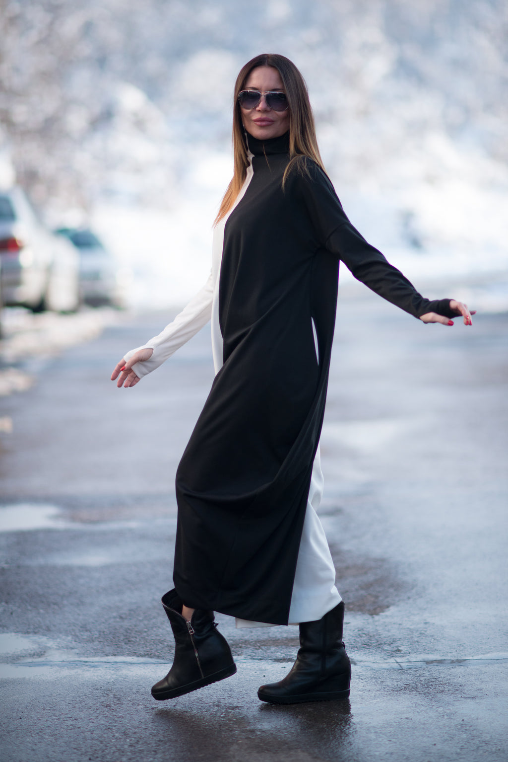 Woman wearing a black and white dress with black boots on a snowy street.