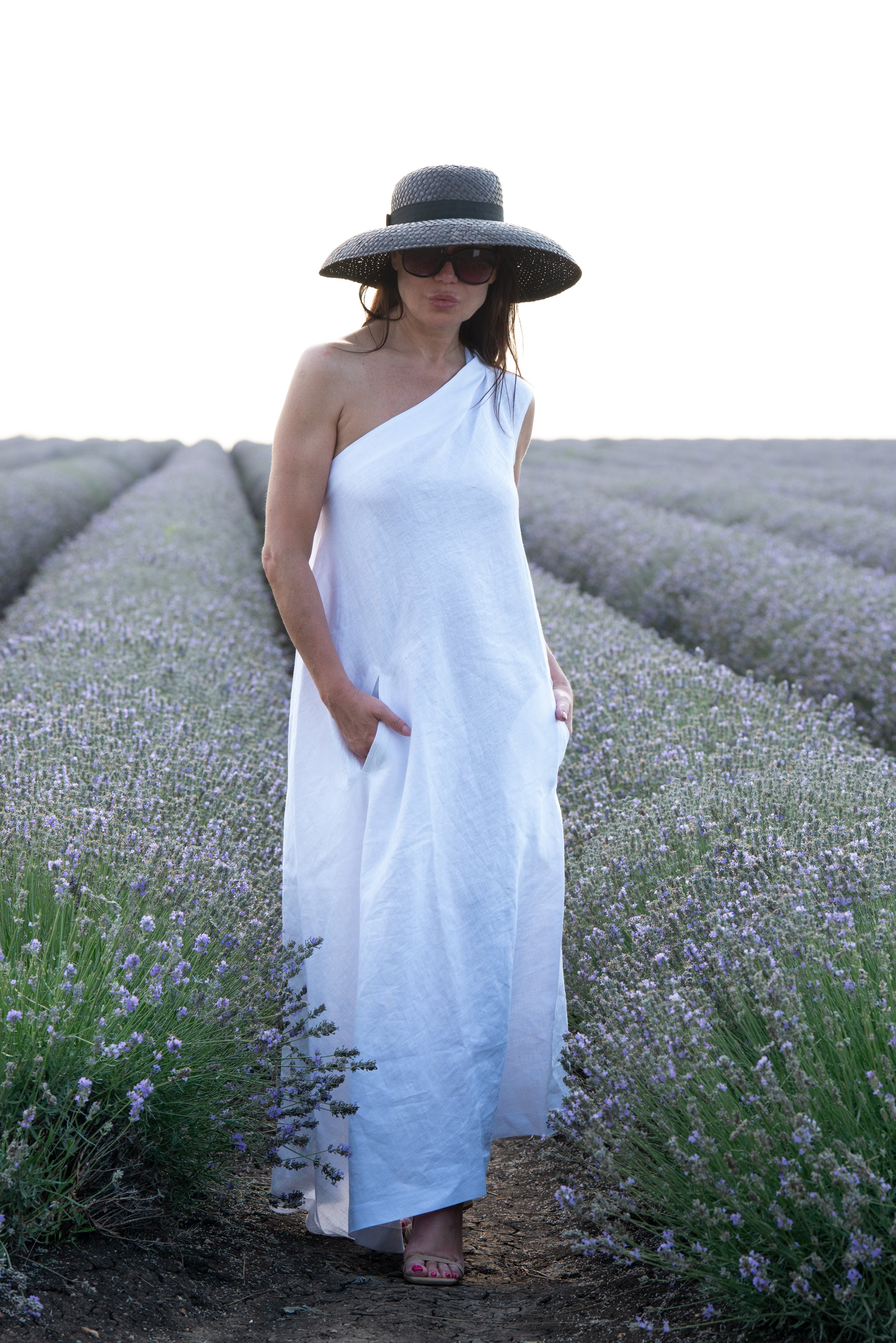 Woman in a white dress and black hat standing in a lavender field.