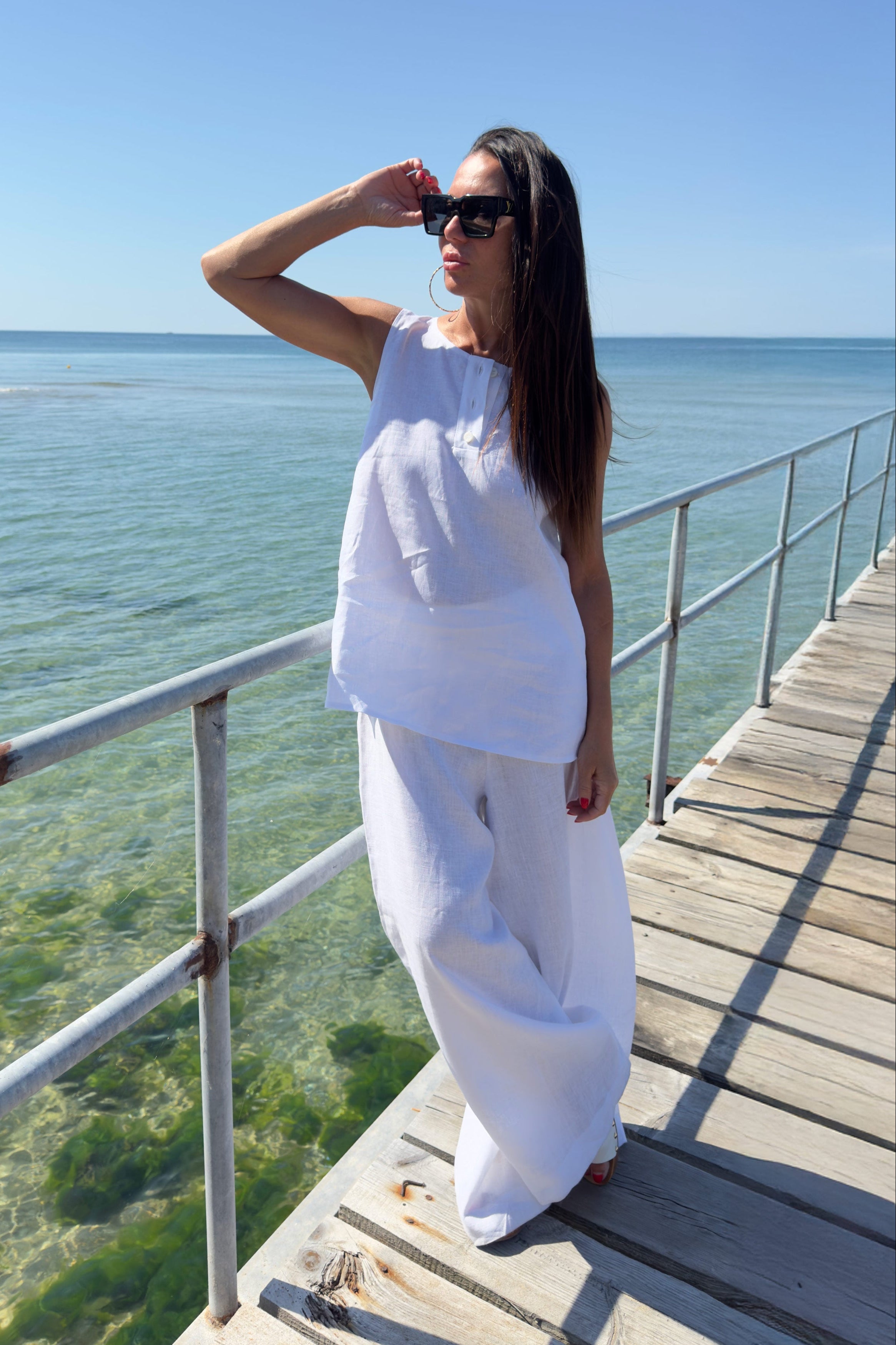 Woman in white outfit standing on a wooden pier by the ocean