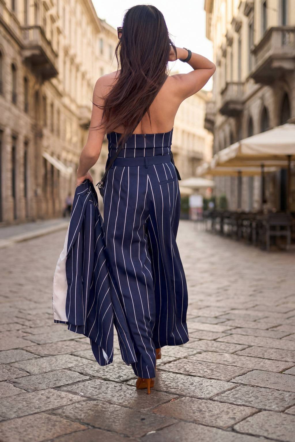 Woman in a blue striped dress walking down a sunlit street.