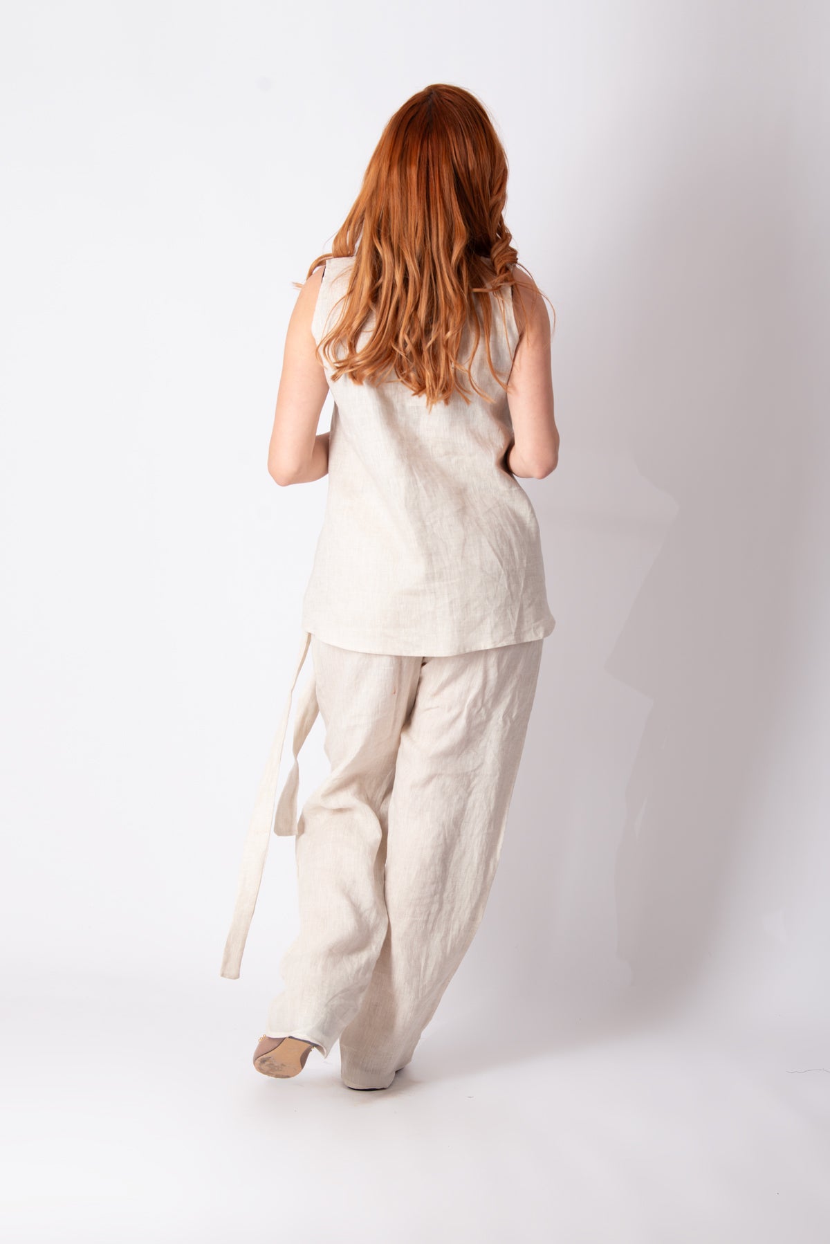 Person wearing a beige sleeveless top and wide-leg pants on a white background