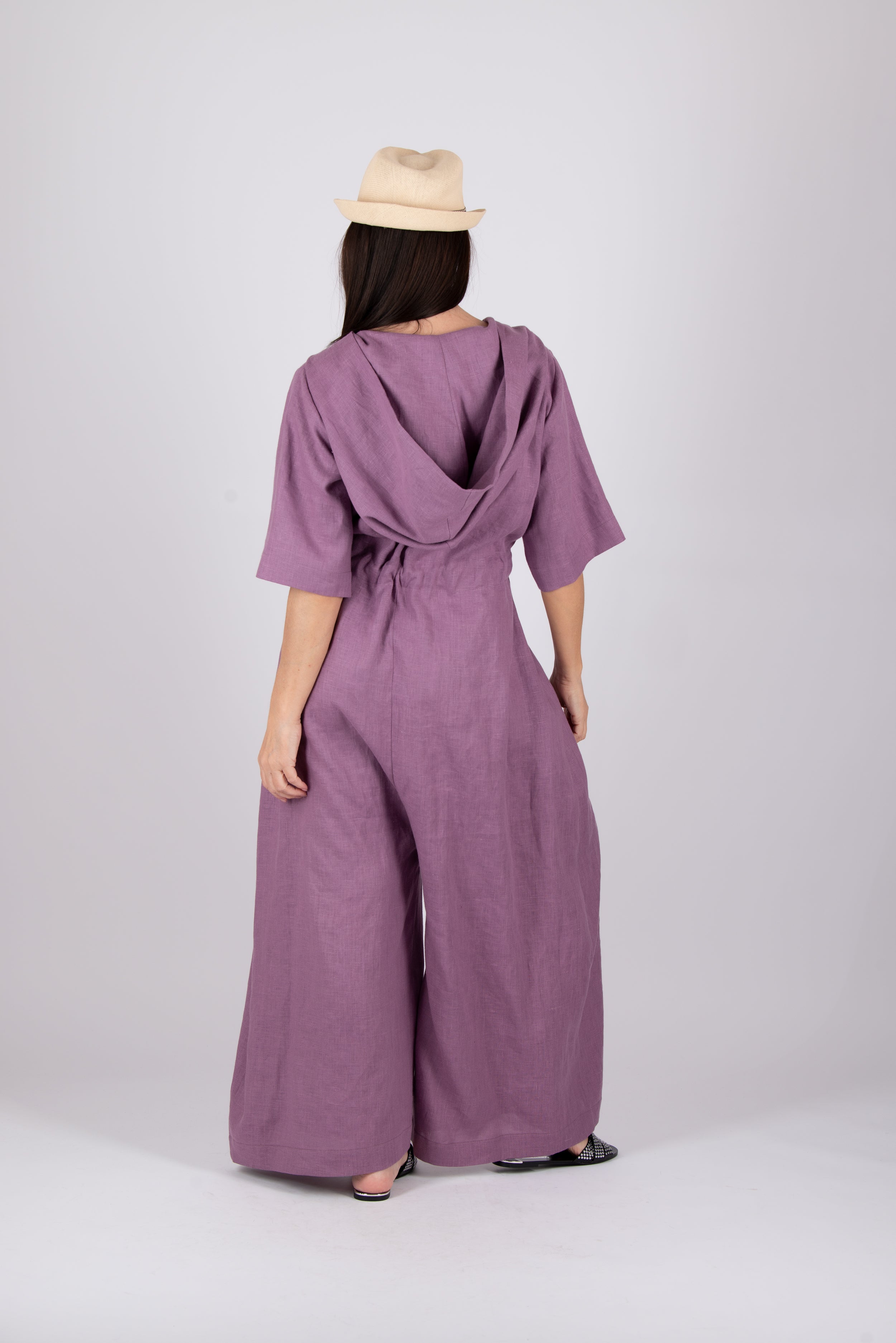 Person wearing a purple jumpsuit with a beige hat on a white background