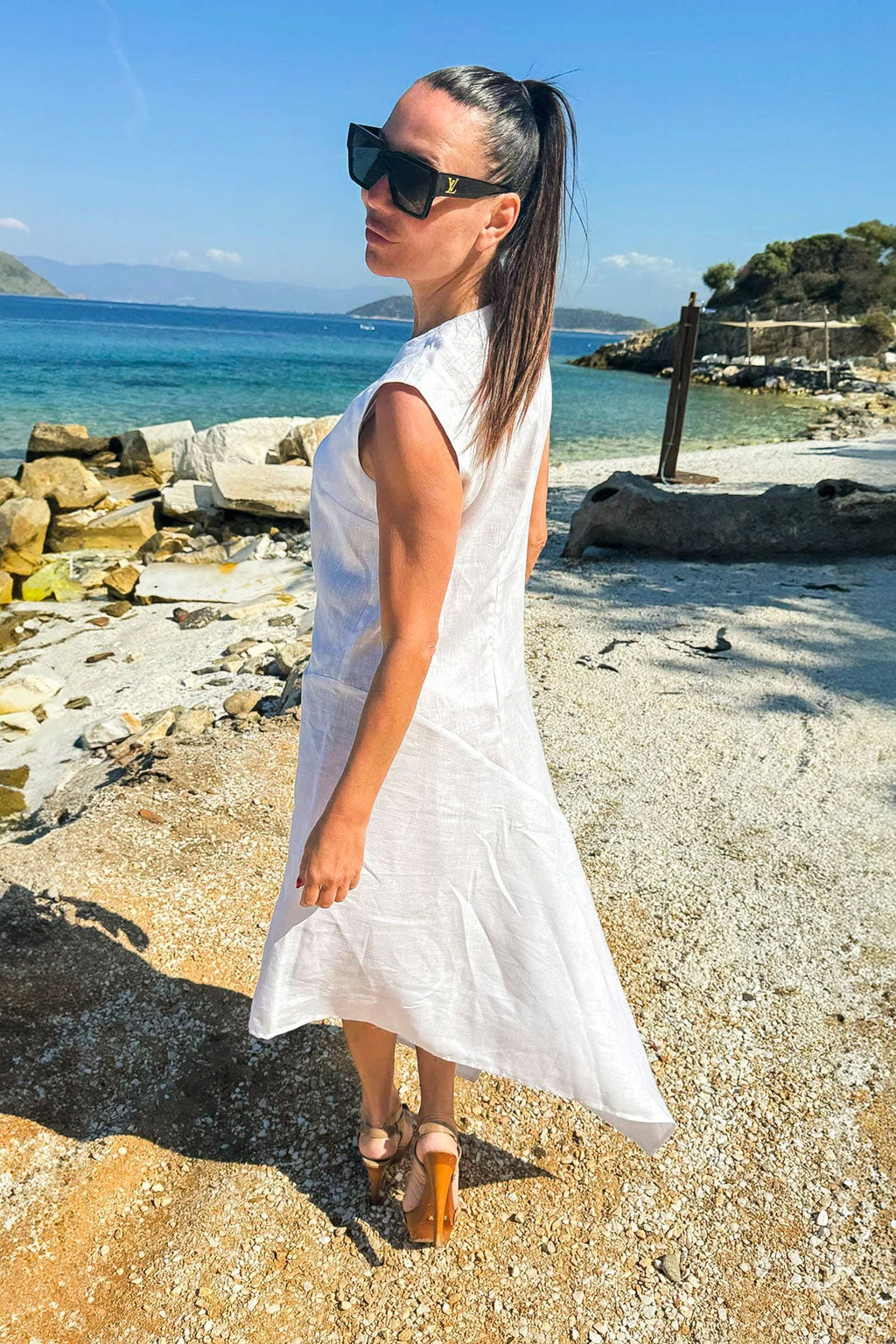 Woman in a white dress standing on a rocky beach with ocean and sky in the background