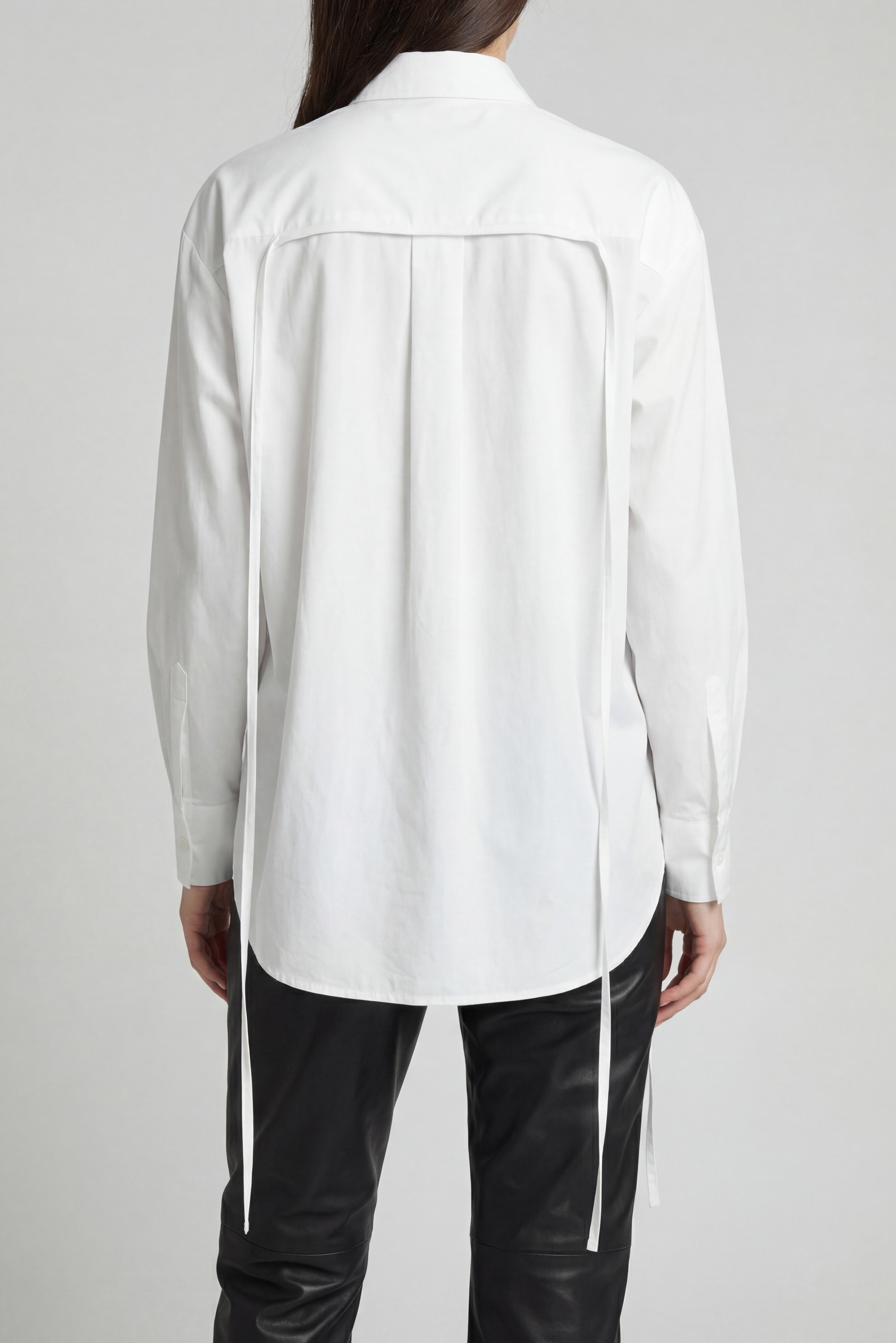 Person wearing a white shirt and black pants on a plain background