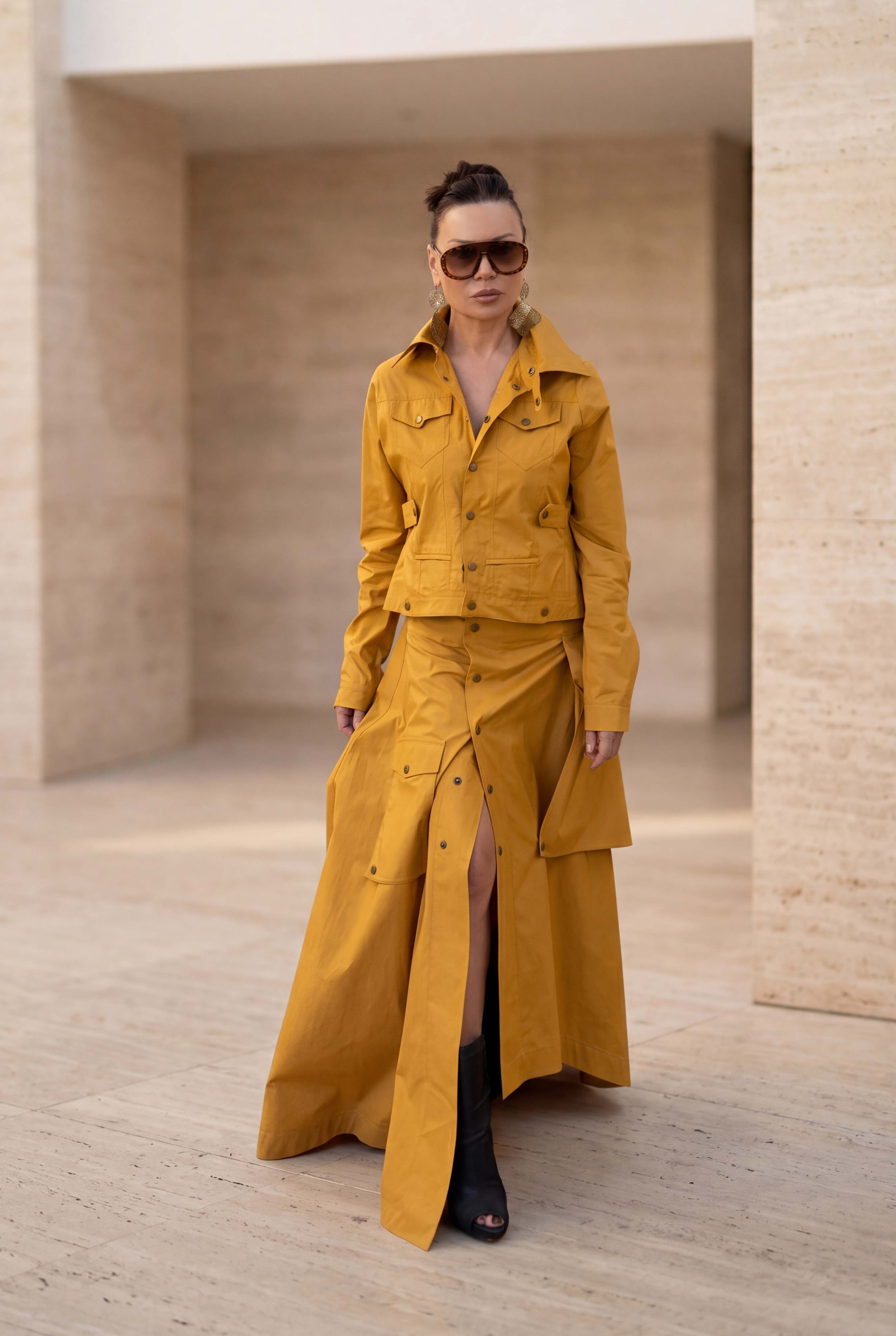 Woman wearing a mustard yellow outfit standing in a minimalist setting.