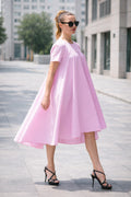 Woman wearing a pink dress and black sunglasses on a city street.