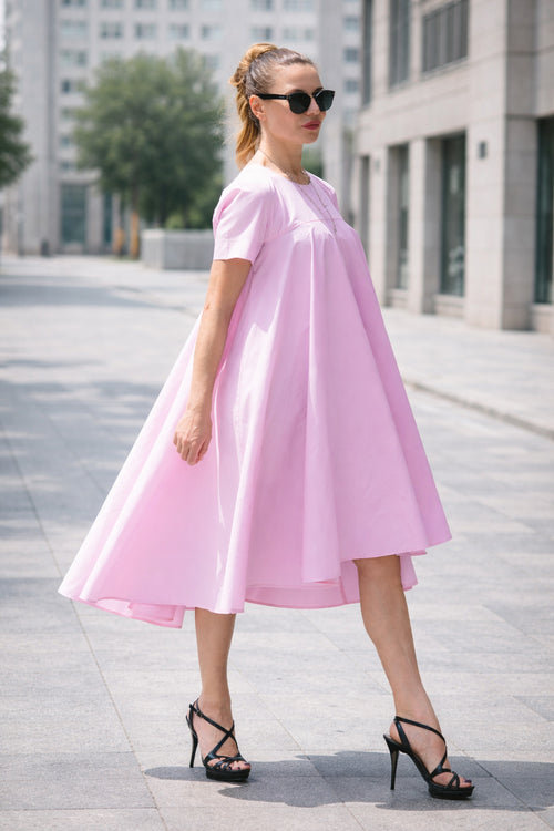 Woman wearing a pink dress and black sunglasses on a city street.