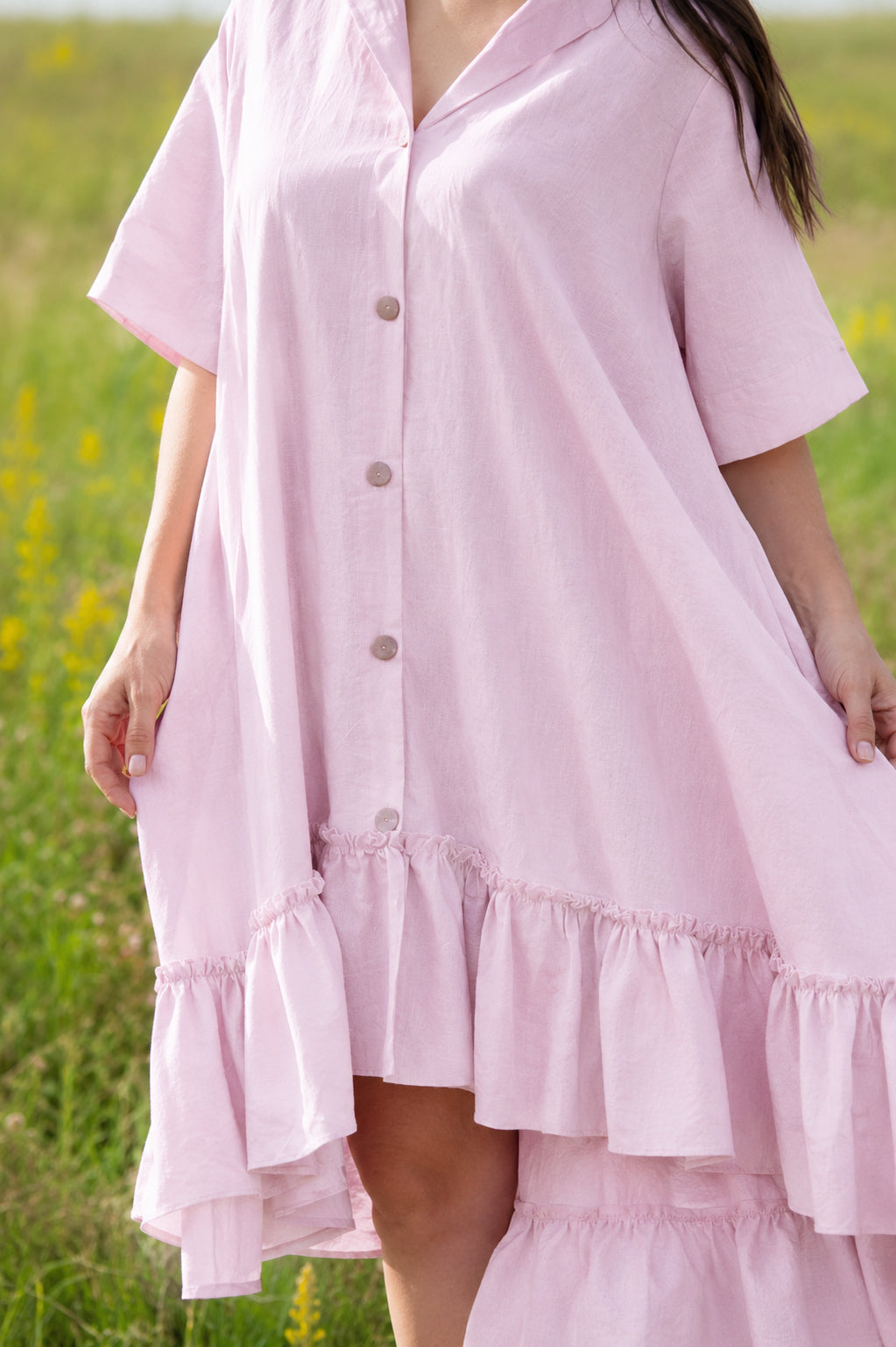 Person wearing a pink dress with ruffled layers in a grassy field.