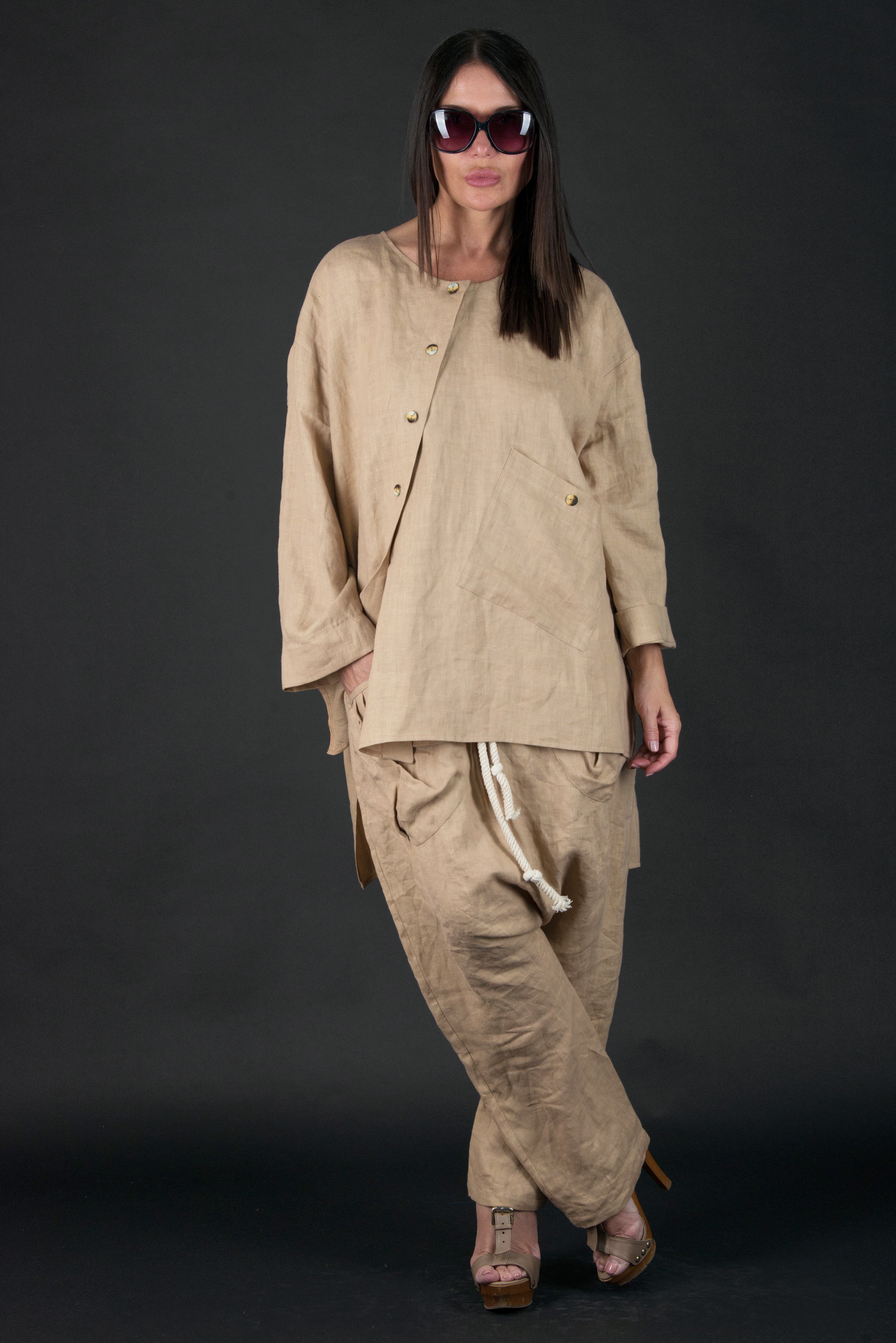 Woman wearing a beige outfit with sunglasses on a black background