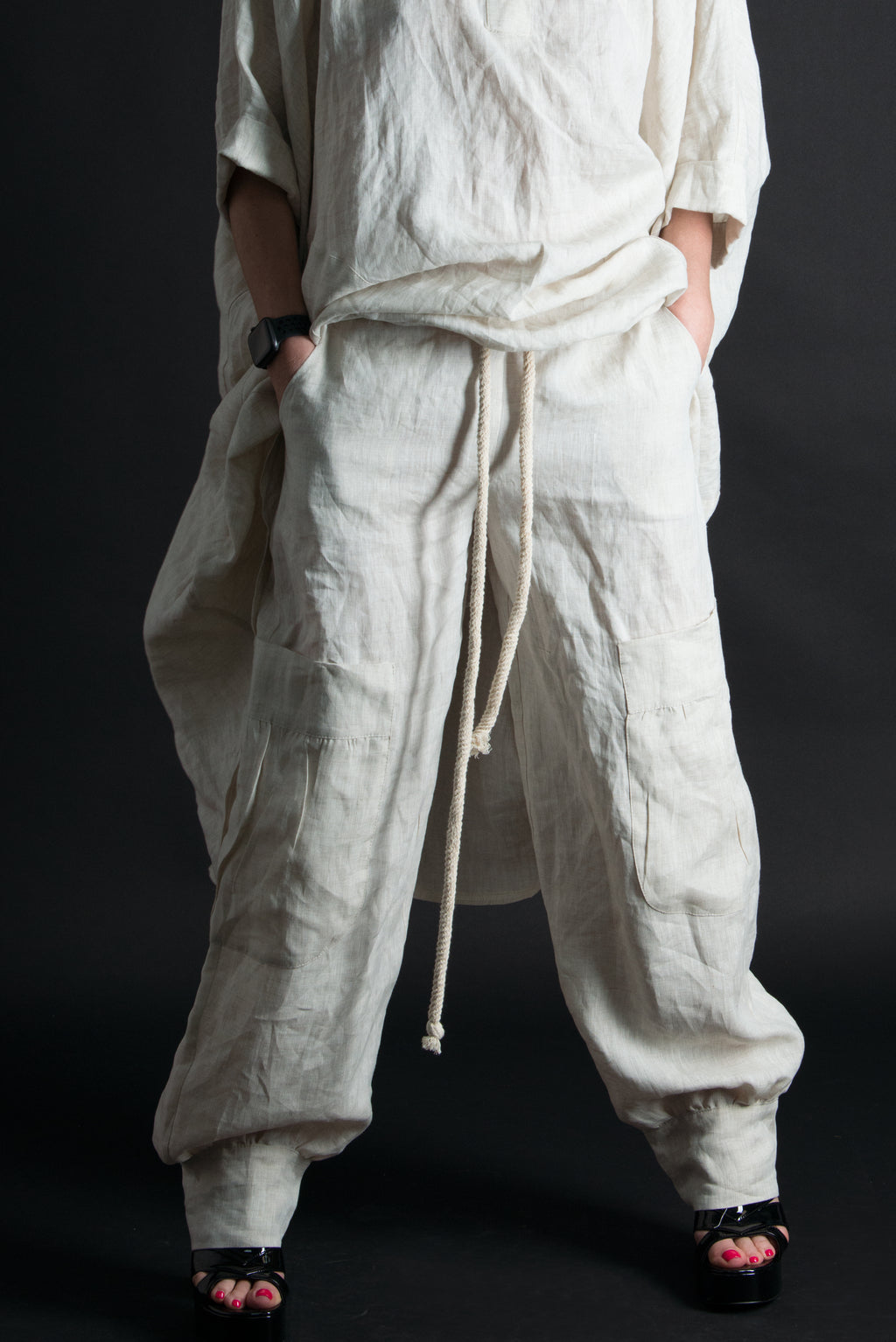 Person wearing a loose-fitting beige linen pants with a drawstring on a black background