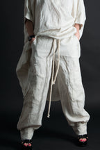 Person wearing a loose-fitting beige linen pants with a drawstring on a black background