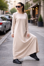 Woman in a long beige dress walking on a city street.