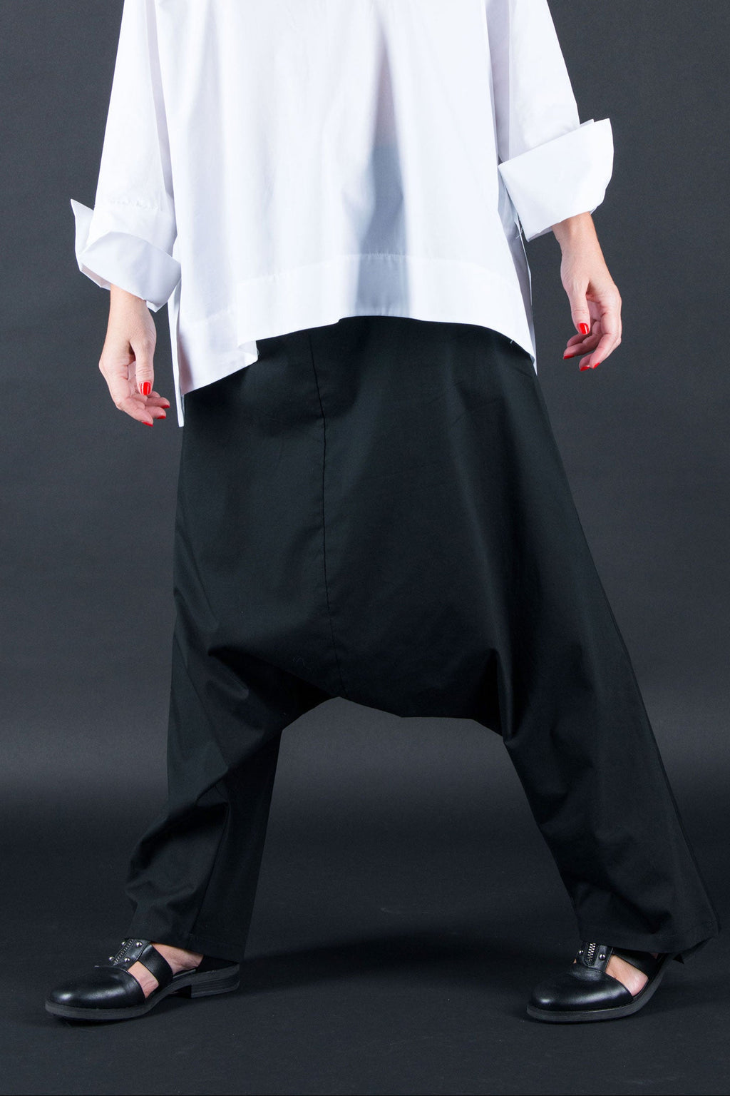 Woman wearing a white oversized shirt and black pants against a dark background