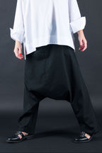 Woman wearing a white oversized shirt and black pants against a dark background