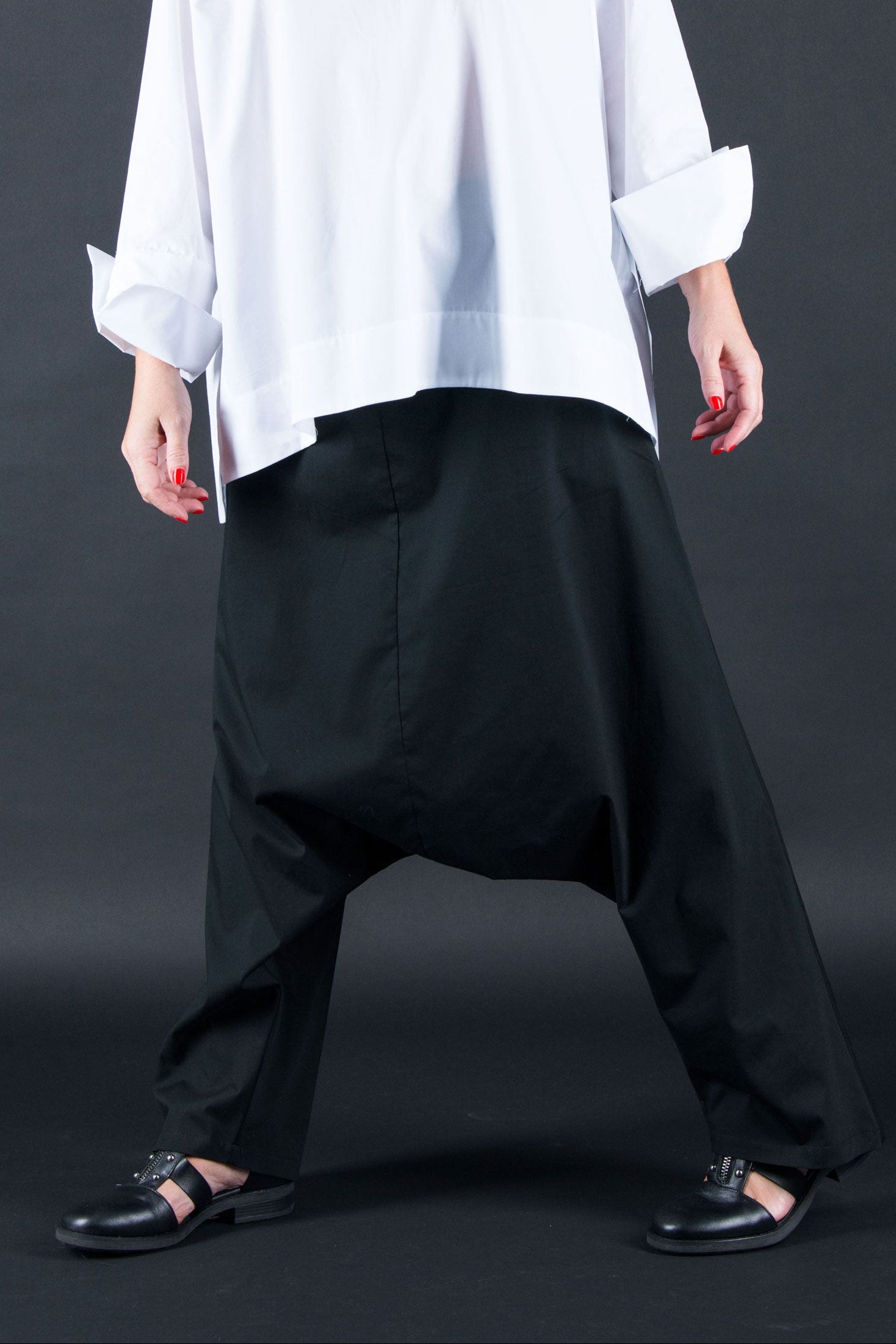 Woman wearing a white oversized shirt and black pants against a dark background