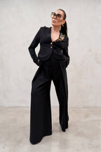 Woman wearing a black outfit with gold accents against a plain background