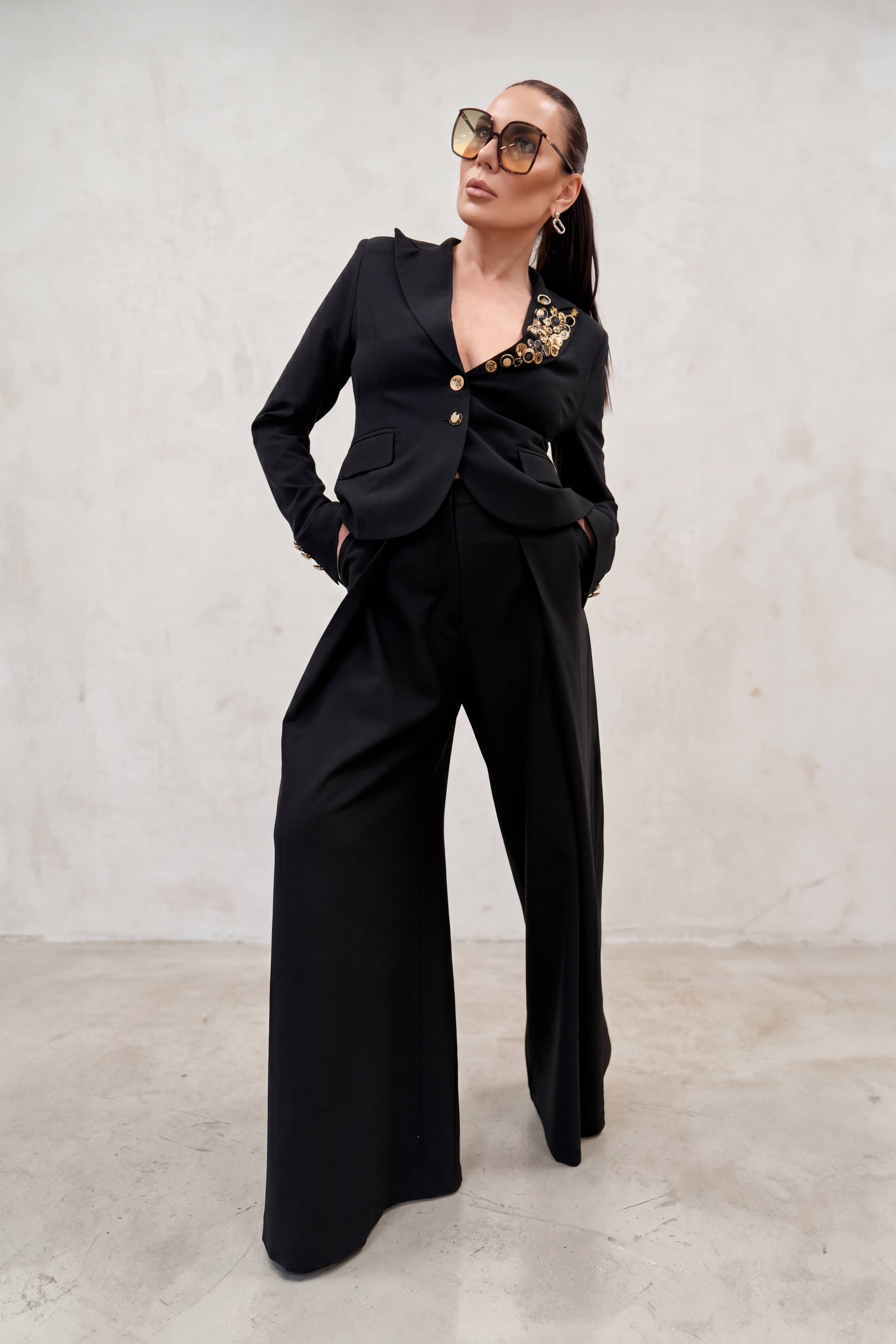 Woman wearing a black outfit with gold accents against a plain background