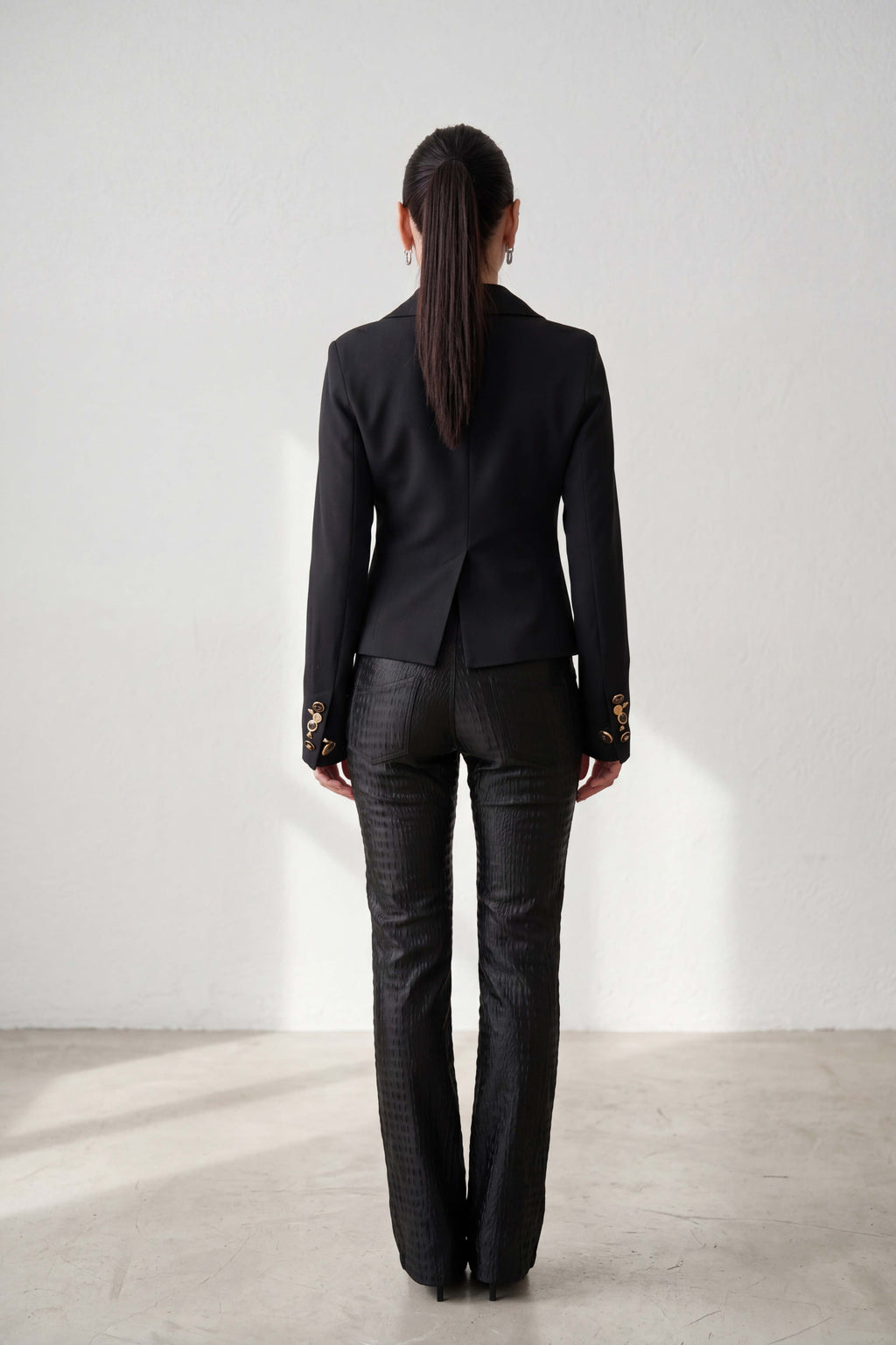 Person wearing a black suit standing against a white wall