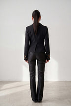Person wearing a black suit standing against a white wall