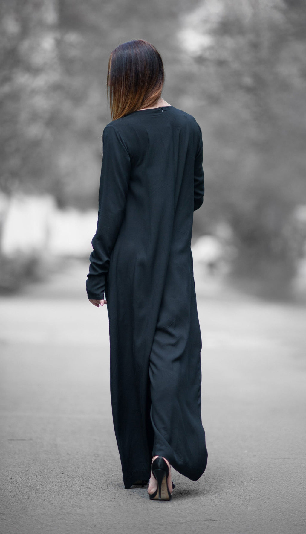 Person wearing a long black dress walking on a path with blurred trees in the background