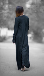 Person wearing a long black dress walking on a path with blurred trees in the background