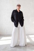 Person wearing a black jacket and white pants in a minimalistic setting