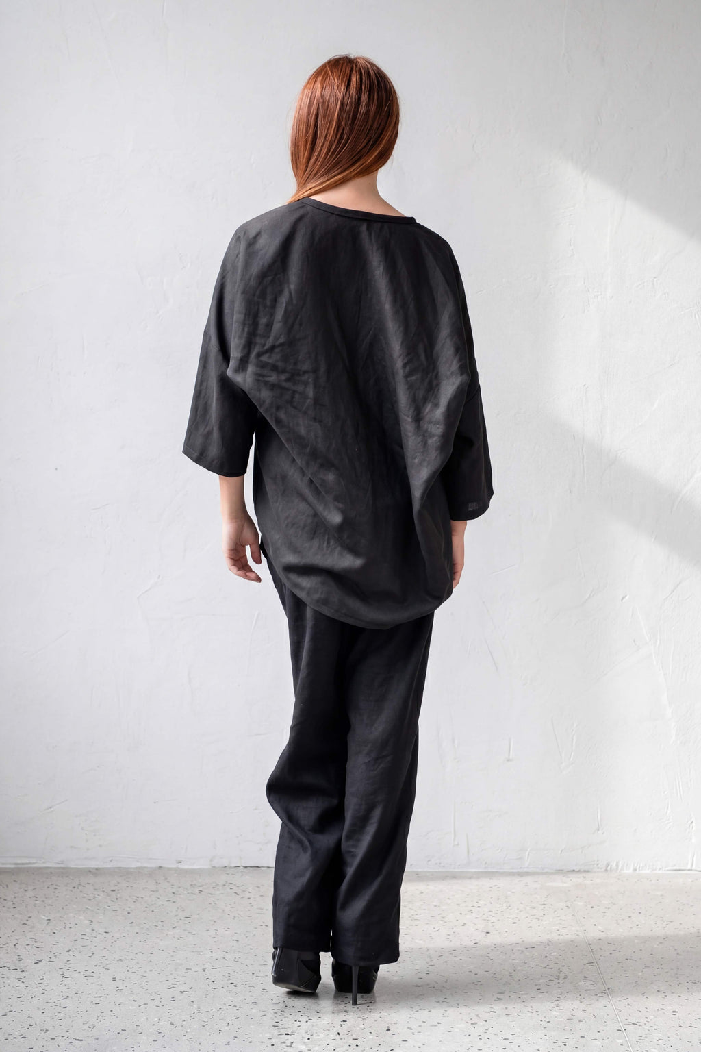 Person wearing a black outfit standing against a white wall