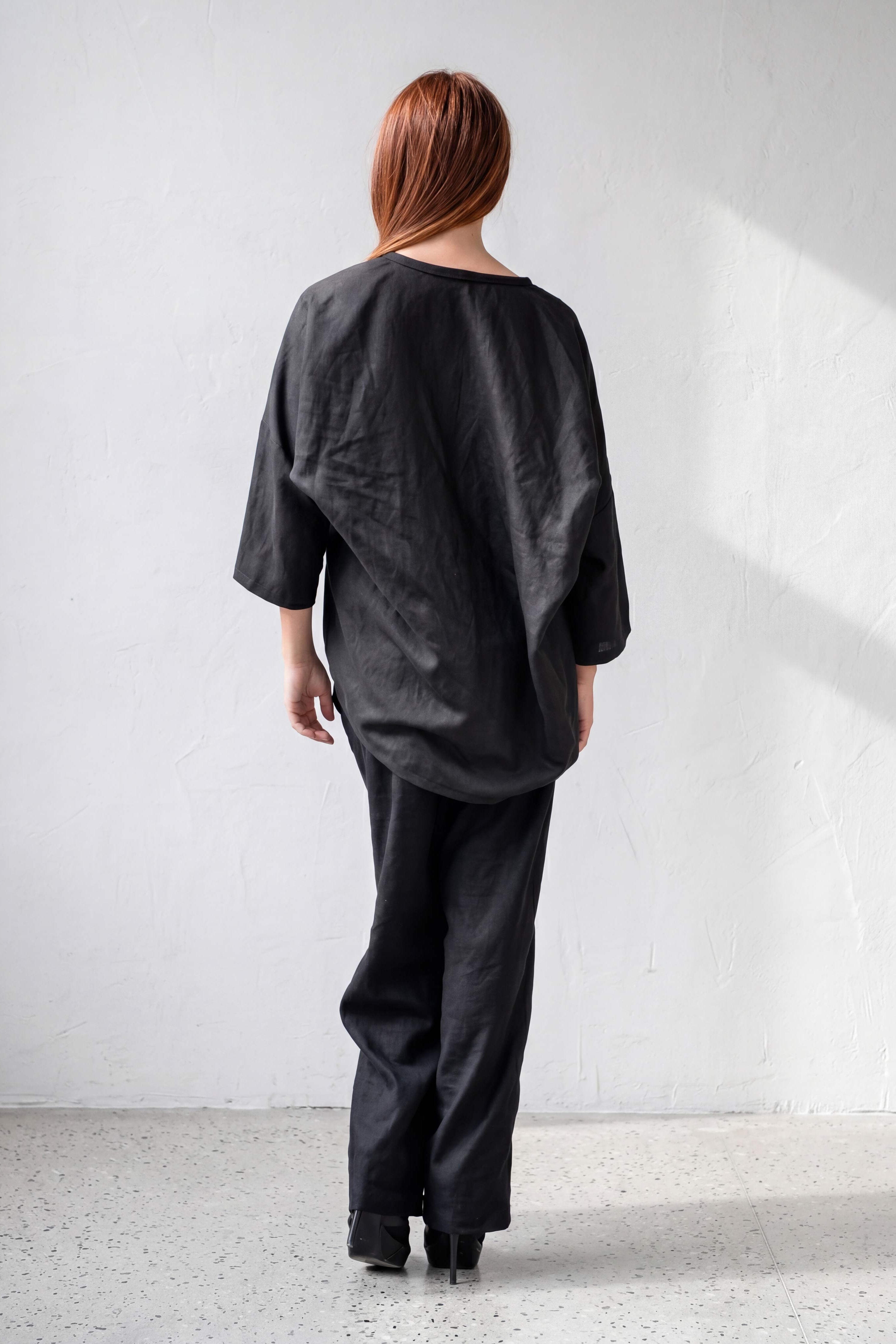 Person wearing a black outfit standing against a white wall