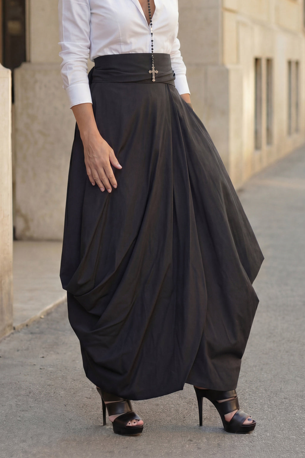 Woman wearing a white blouse and black drapey skirt on a city street.