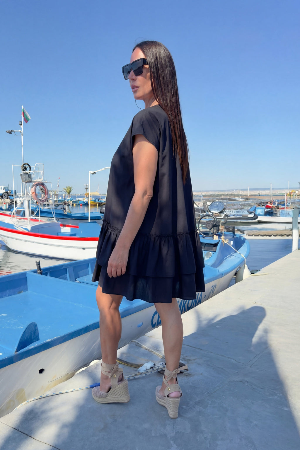 Woman in a black dress standing on a dock with boats in the background