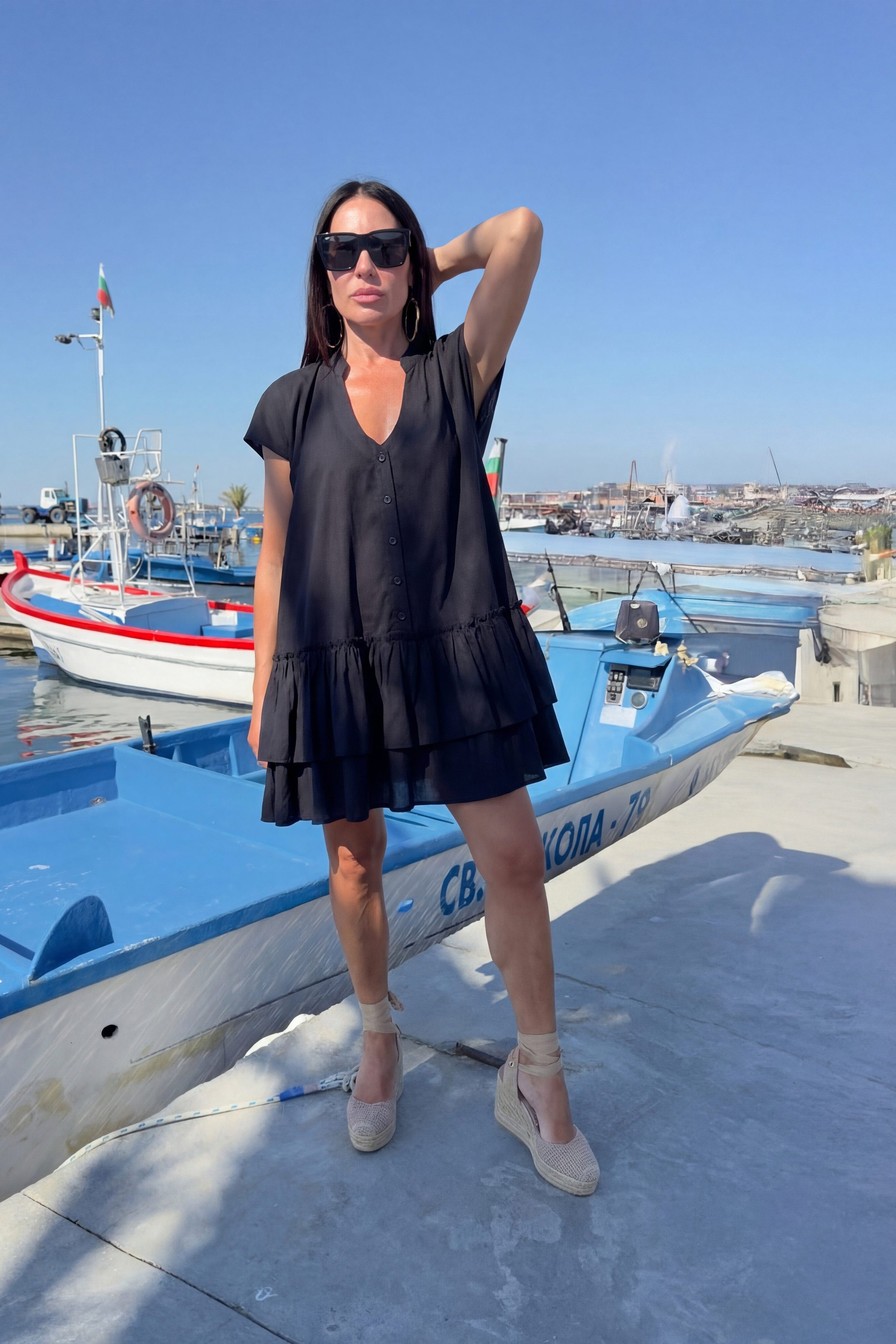 Woman in a black dress standing on a dock with boats in the background