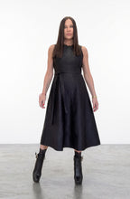 Woman wearing a black sleeveless dress with a fitted bodice and flared skirt on a white background.