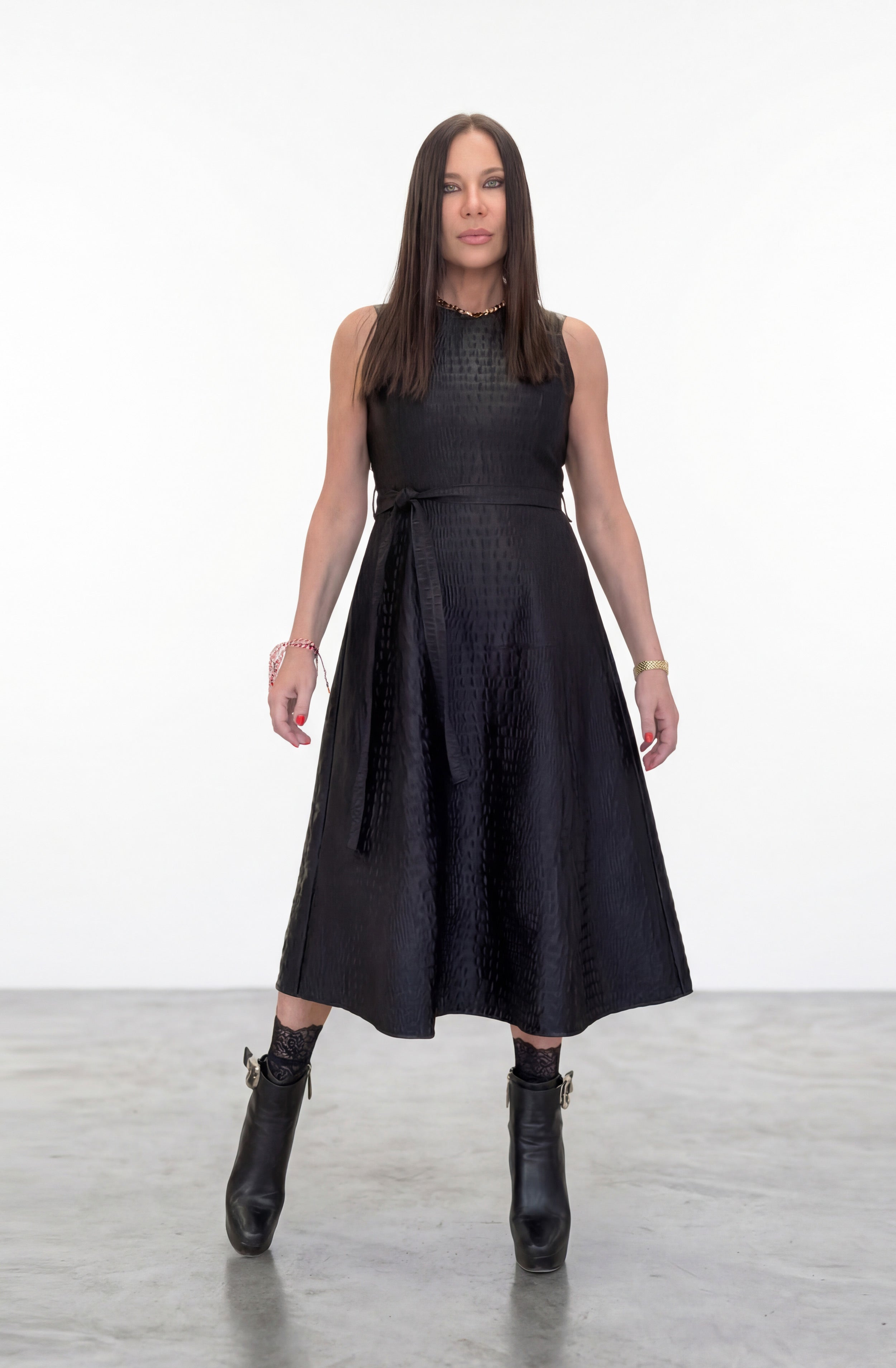 Woman wearing a black sleeveless dress with a fitted bodice and flared skirt on a white background.