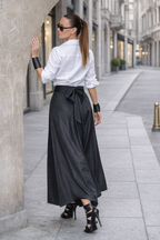 Woman in a white shirt and black skirt standing on a city street.