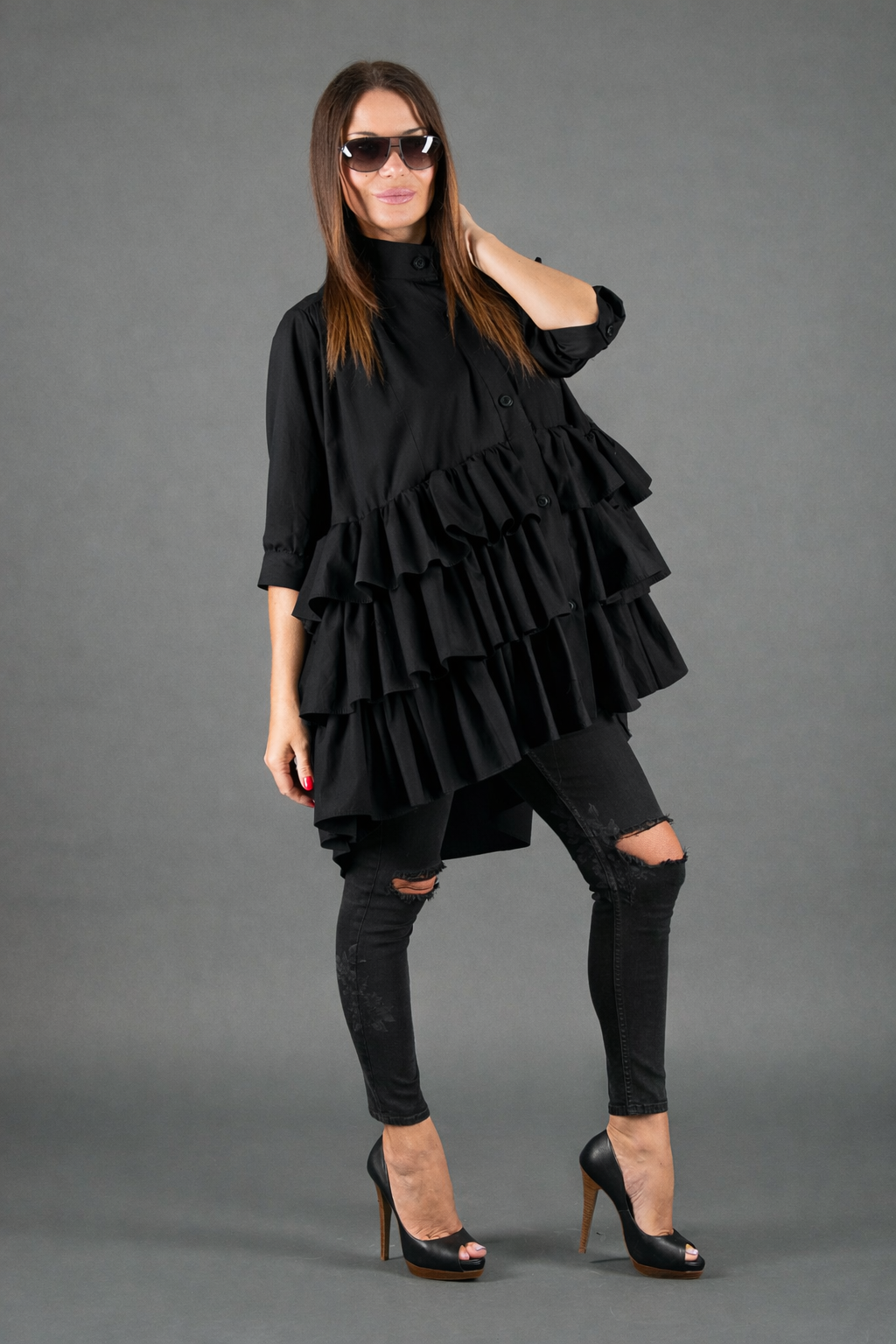 Woman wearing a black ruffled dress with ripped jeans against a gray background