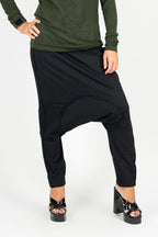 Person wearing a green long-sleeve top and black harem pants on a white background