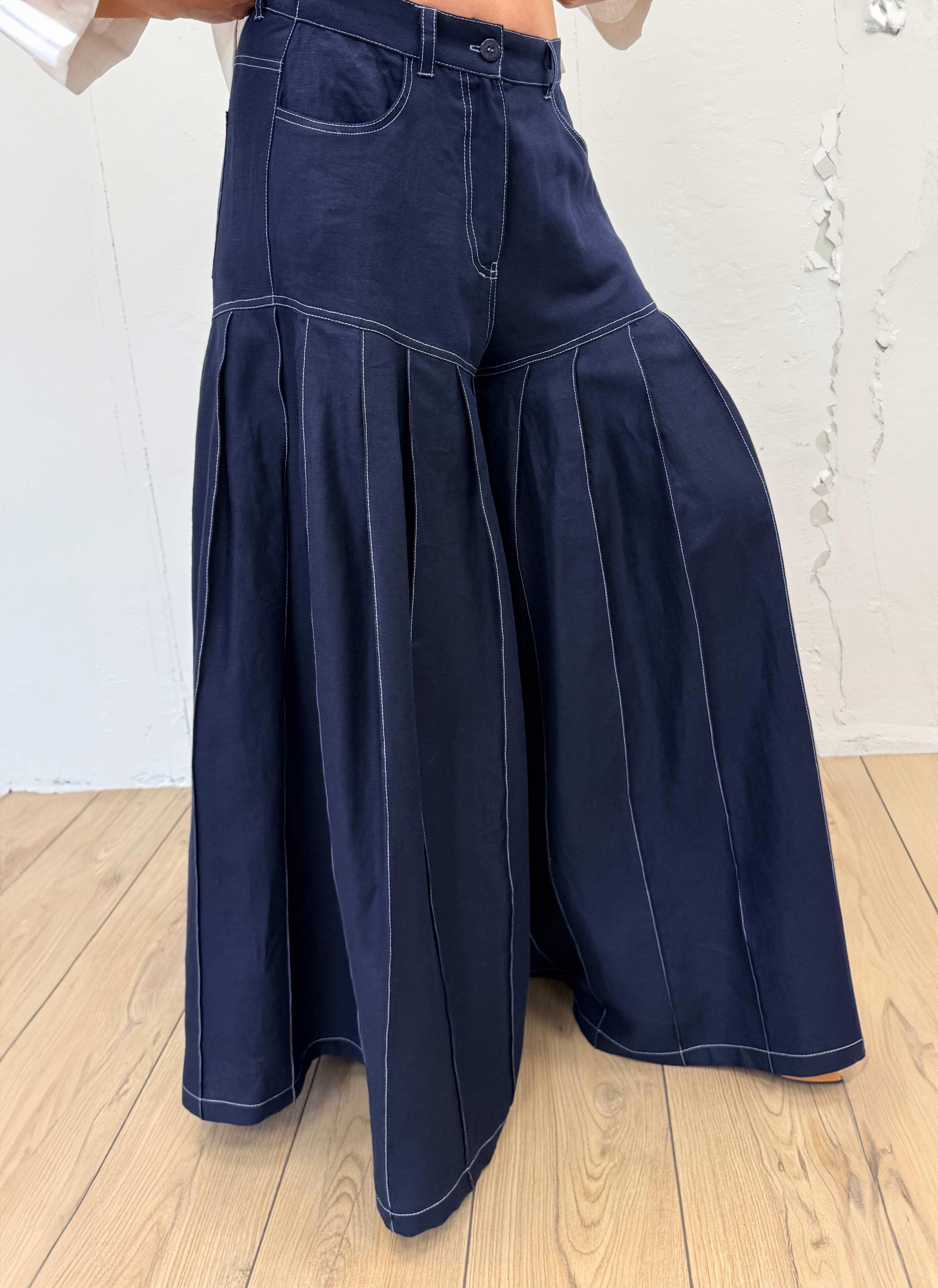 Navy blue wide-leg jeans worn by a person on a wooden floor with a white wall background