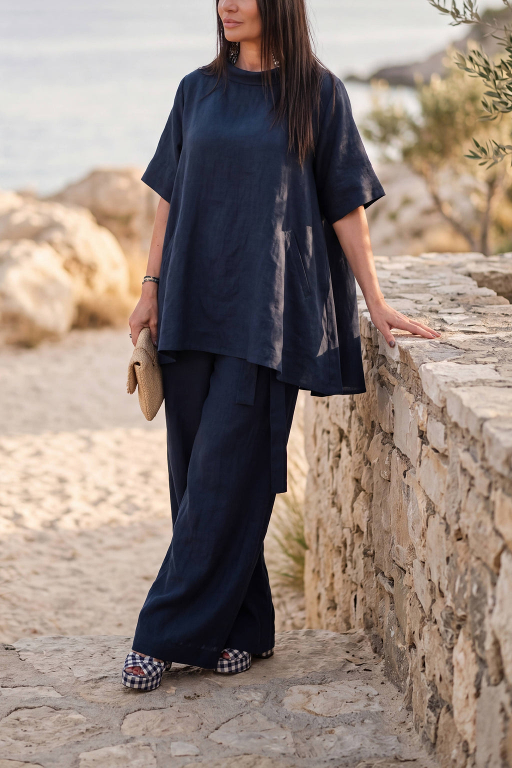 Woman in navy outfit standing by a stone wall with scenic background