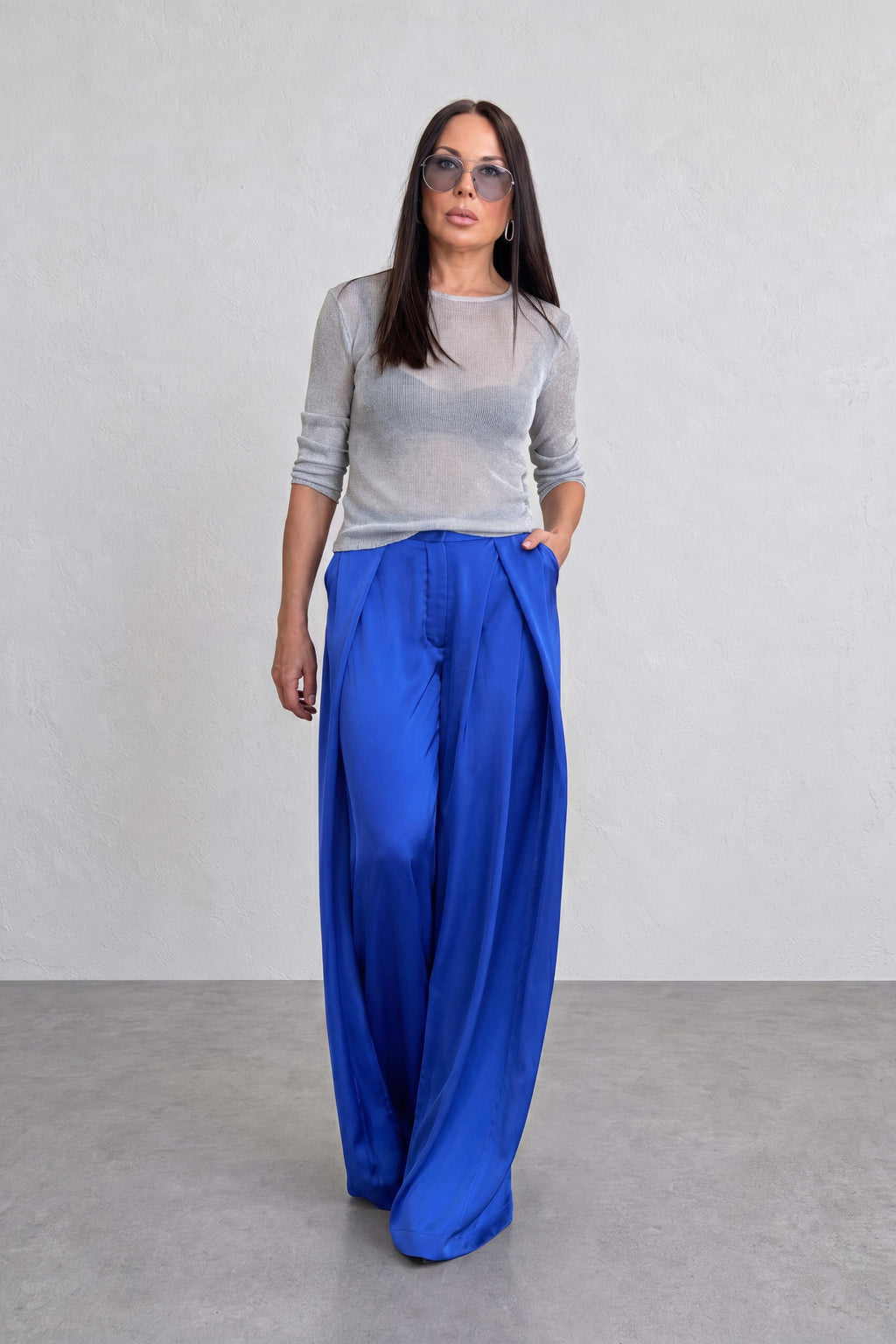 Woman wearing a gray top and blue pants against a plain background