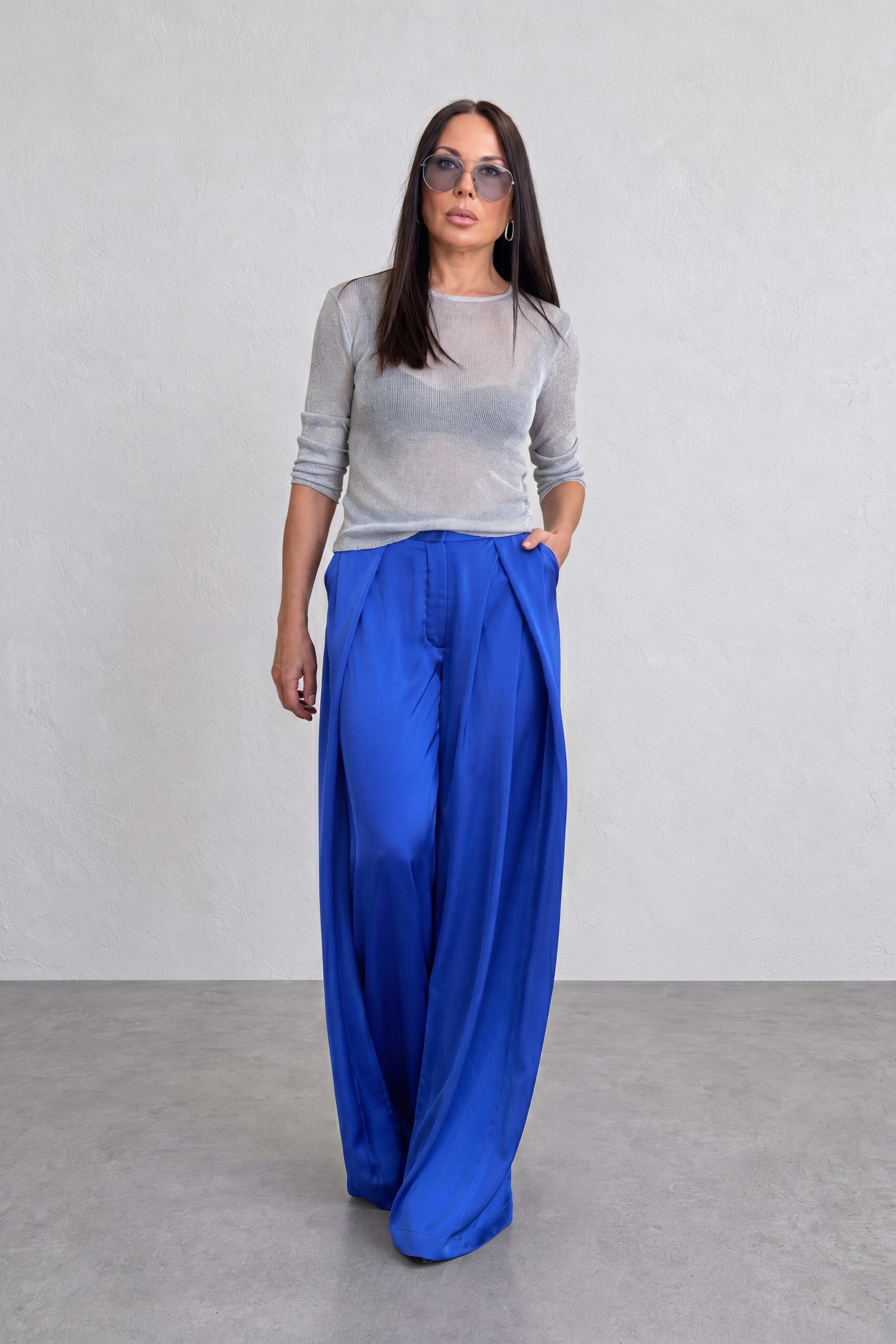 Woman wearing a gray top and blue pants against a plain background
