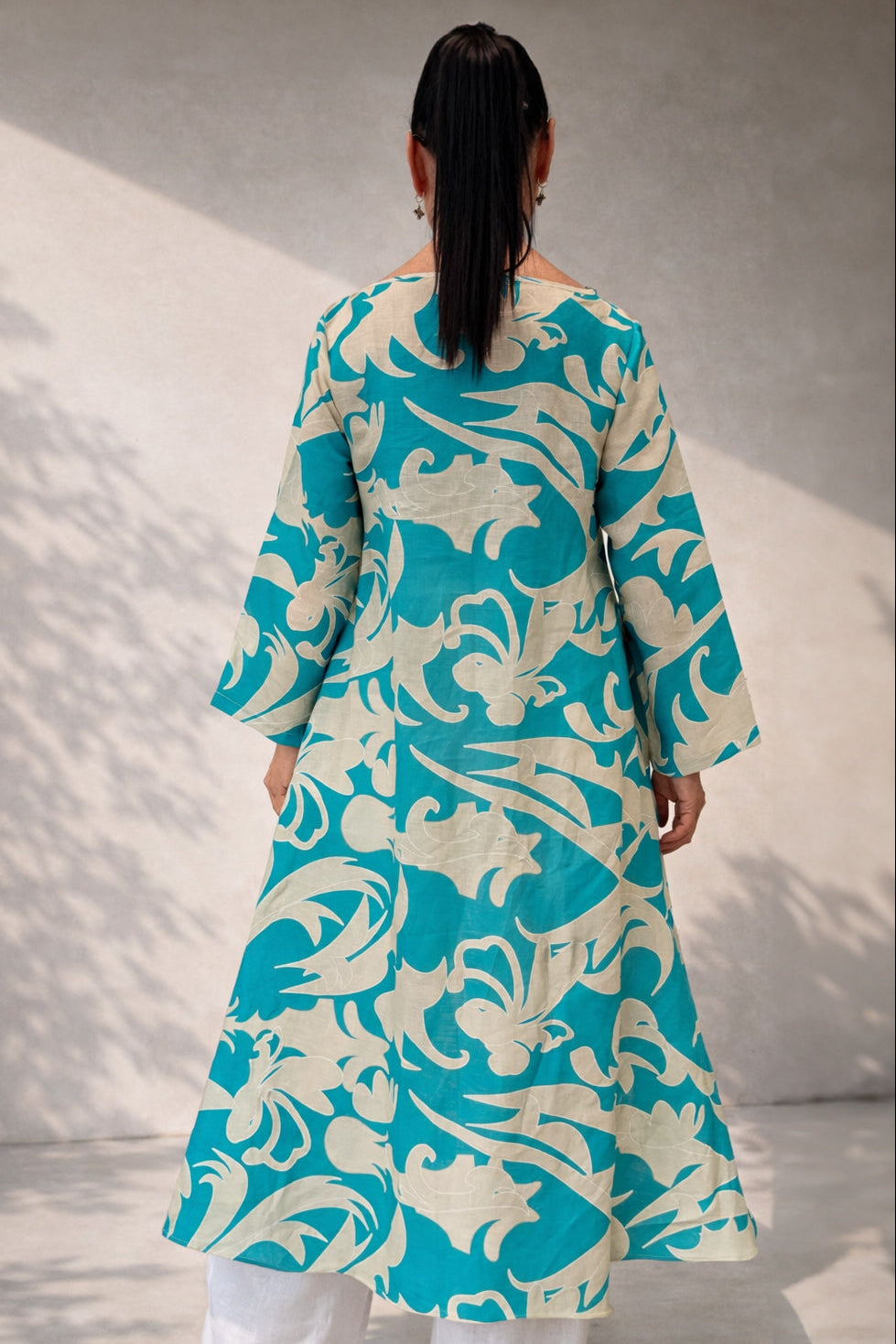 Person wearing a turquoise and white patterned kurta with white pants against a neutral background