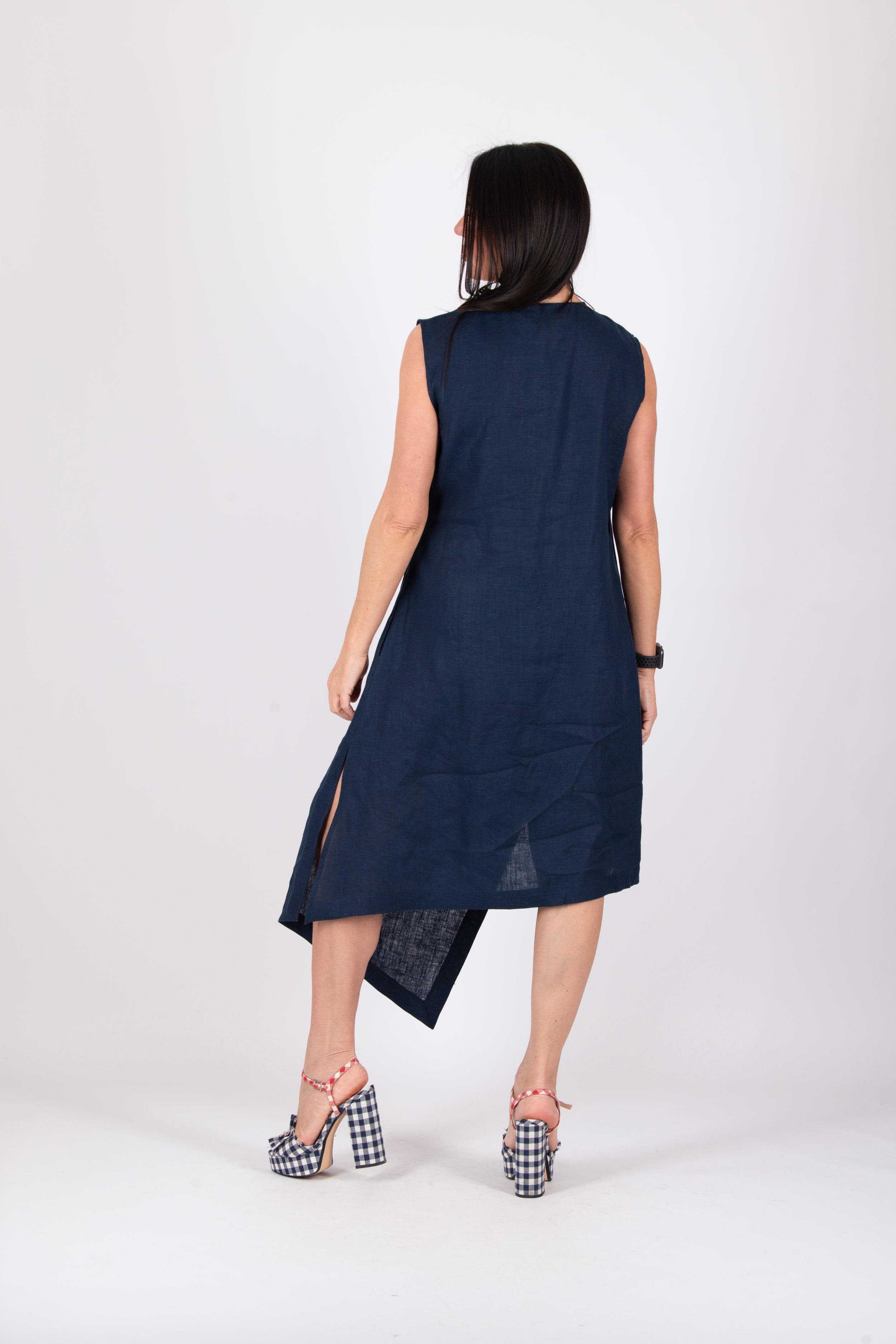 Woman wearing a navy sleeveless dress with a slit on a white background