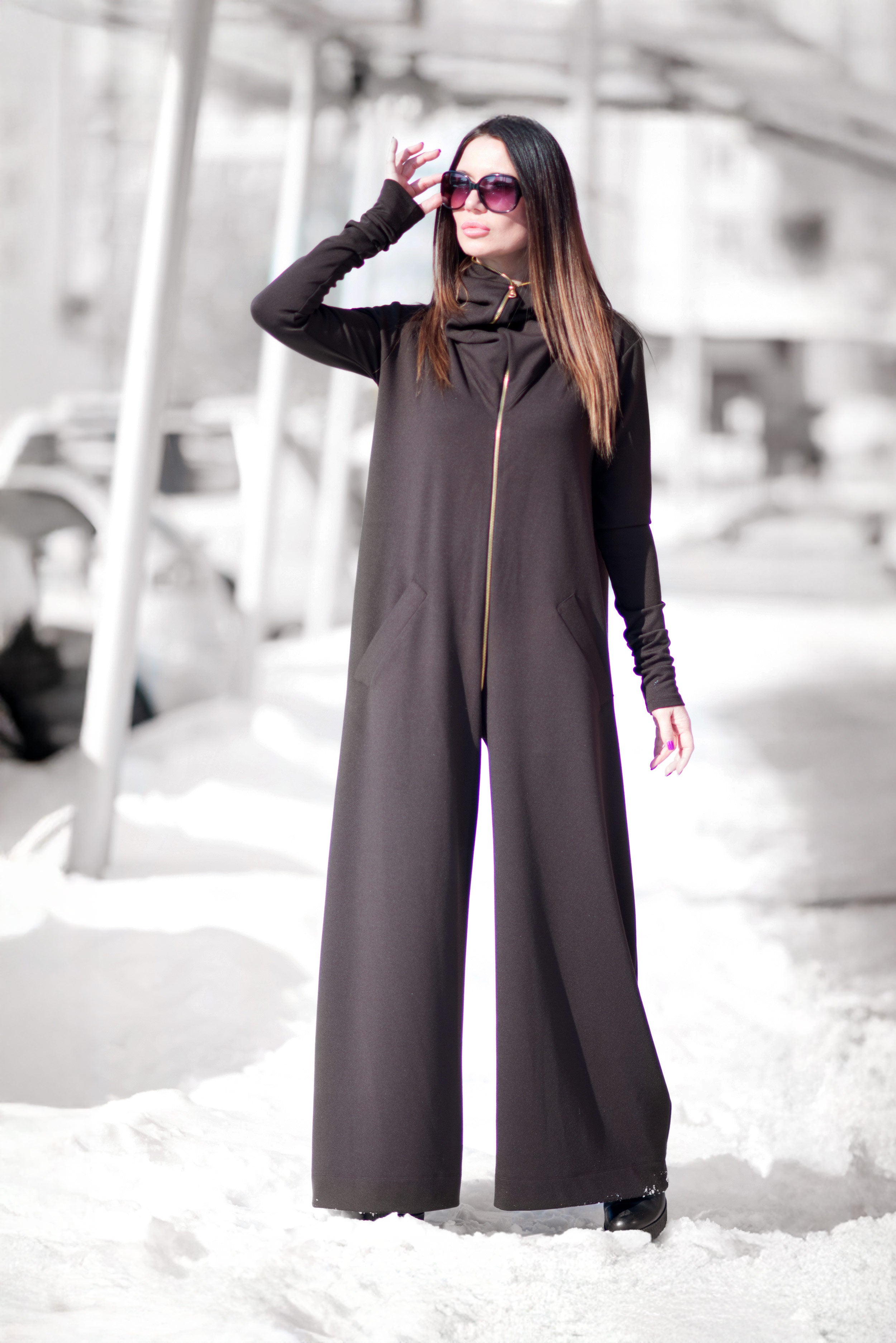 Woman wearing a long dark gray jumpsuit standing in a snowy landscape.