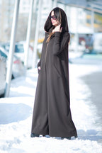 Person wearing a long black coat standing in a snowy area.