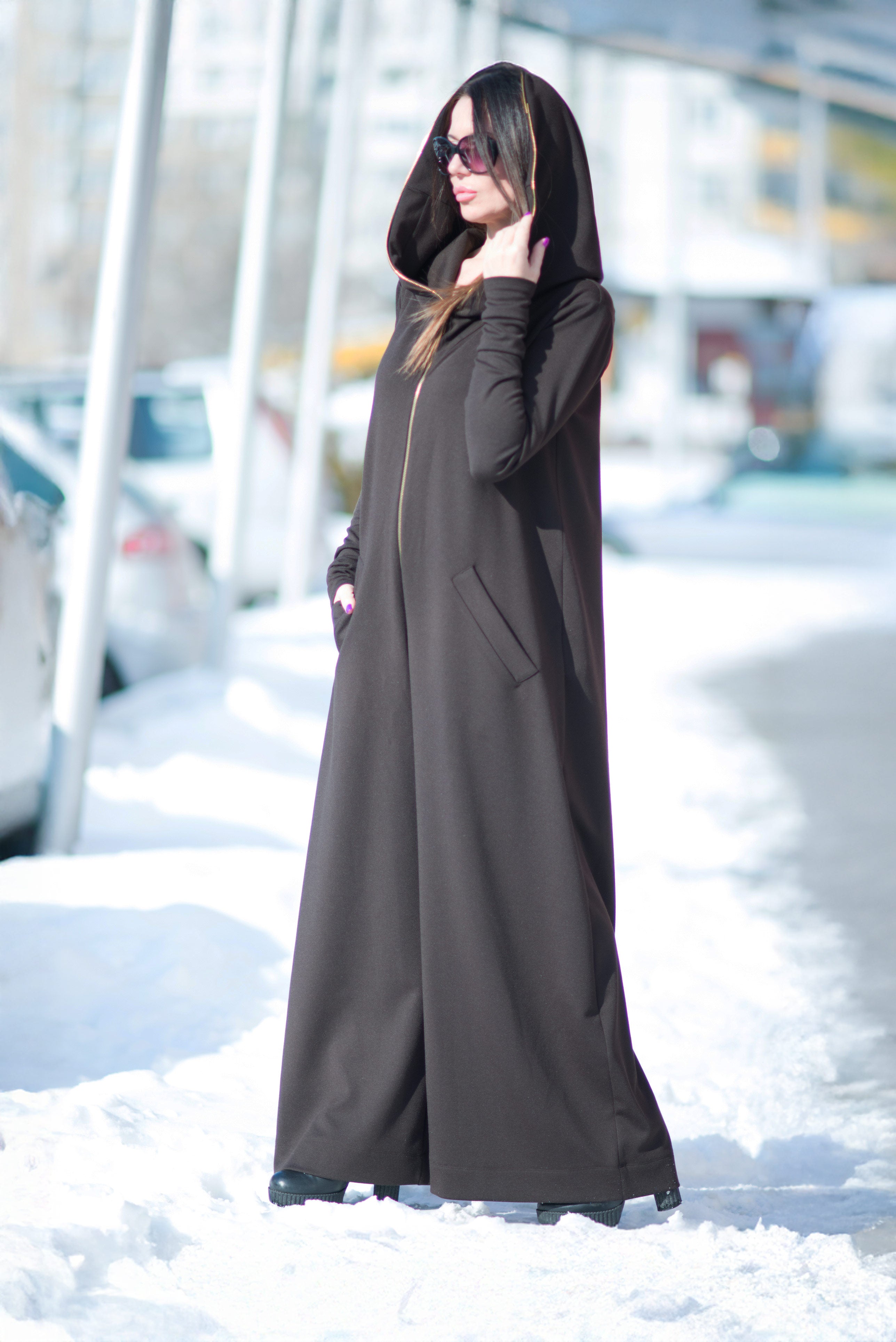 Person wearing a long black coat standing in a snowy area.