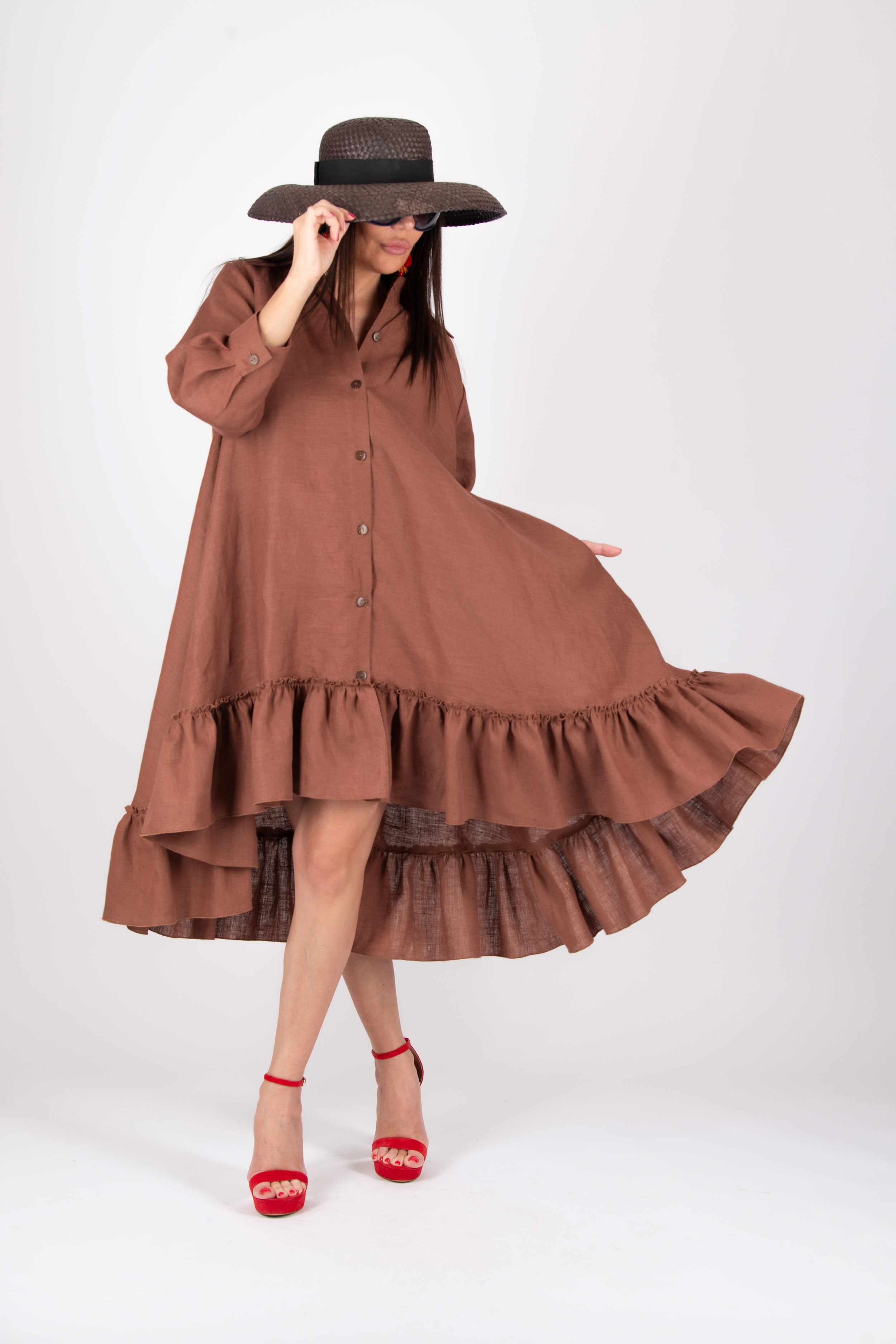 Woman wearing a brown linen dress with ruffles and a wide-brimmed hat on a white background