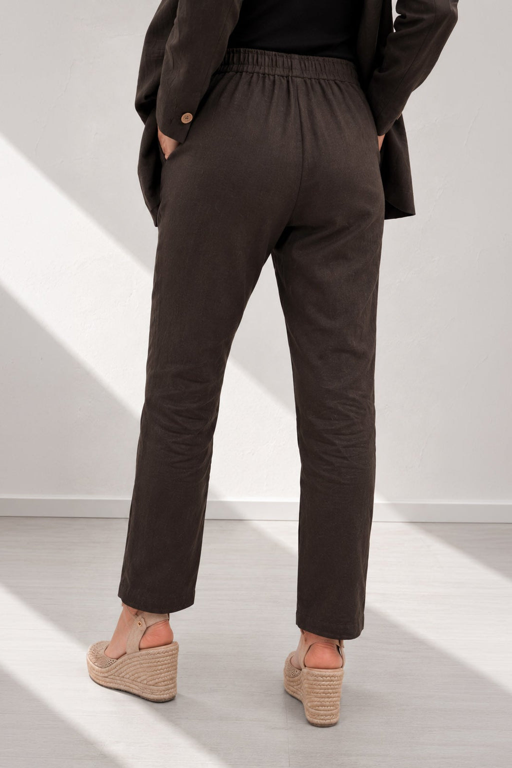 Person wearing dark brown pants and a coat in a minimalistic setting