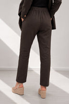 Person wearing dark brown pants and a coat in a minimalistic setting