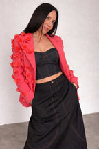 Woman wearing a pink blazer with floral embellishments and a black outfit against a white background