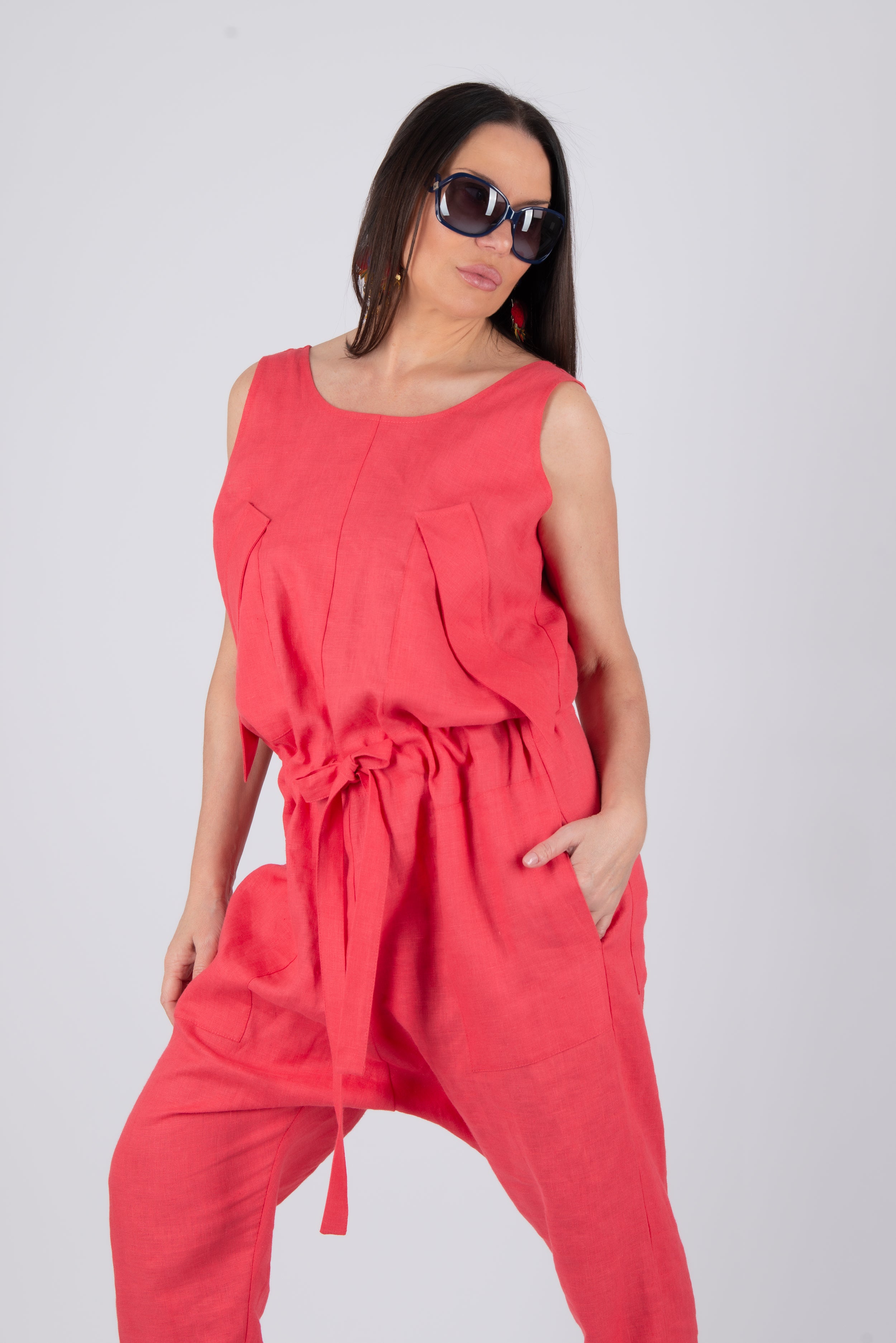 Woman wearing a red sleeveless top and pants with sunglasses on a plain background